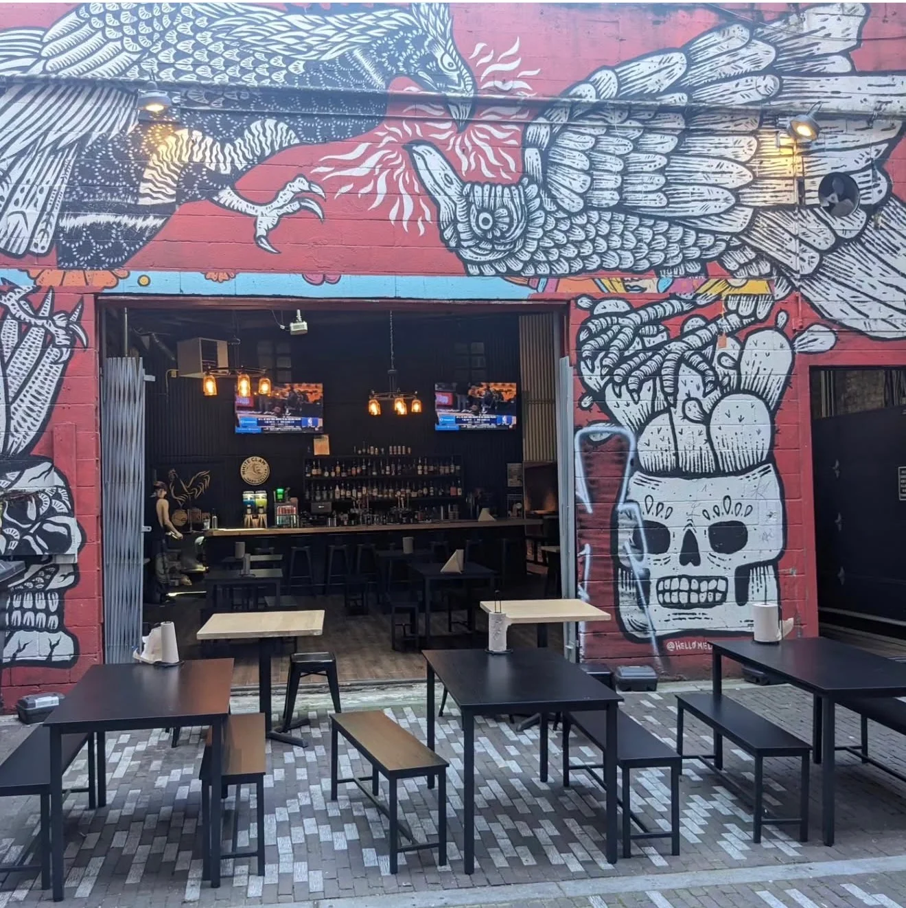 An outdoor dining area featuring vibrant street art on the wall, with tables arranged for customers.