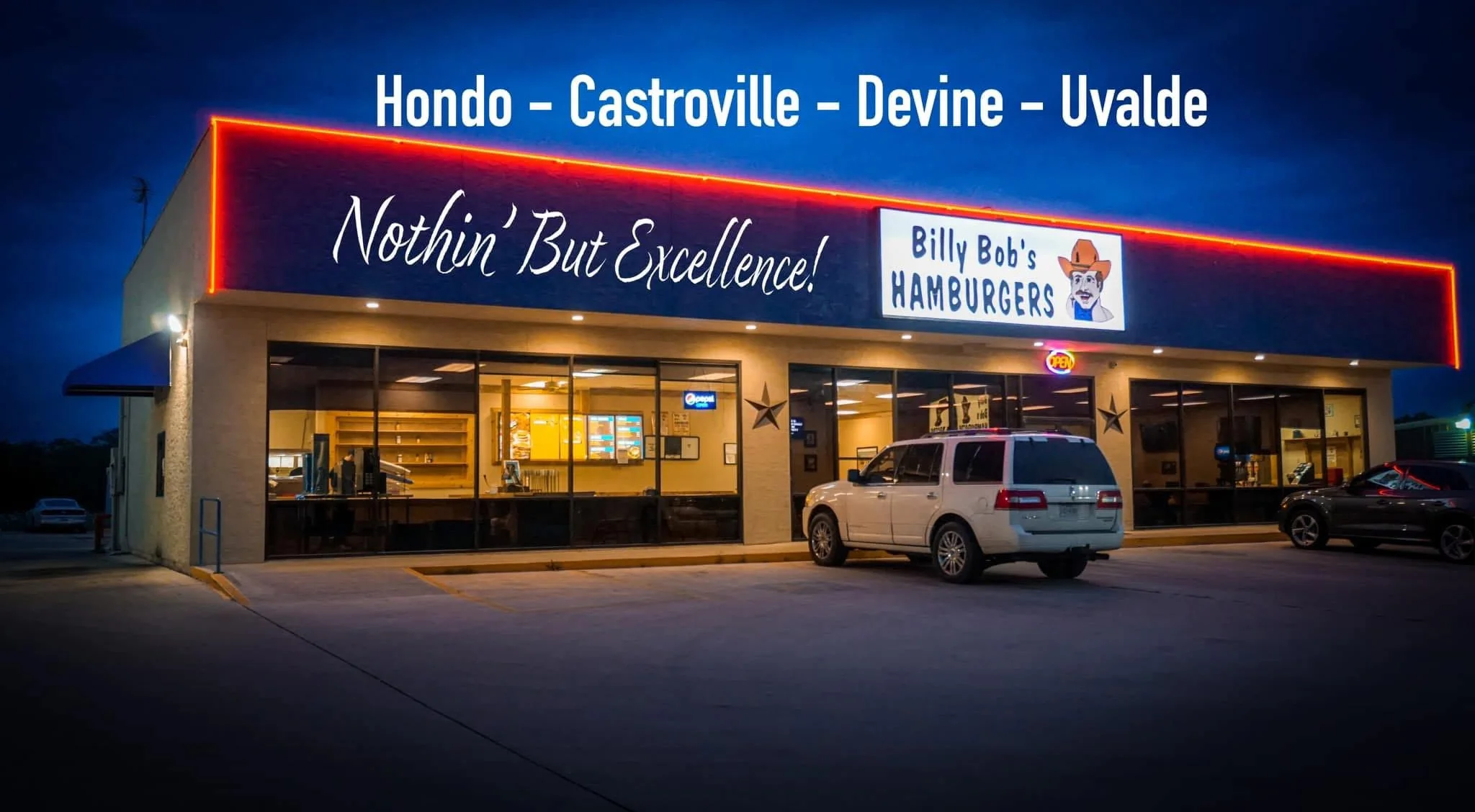 An exterior view of a hamburger restaurant with a 'Now Hiring' sign in front. The building has a rustic appearance.
