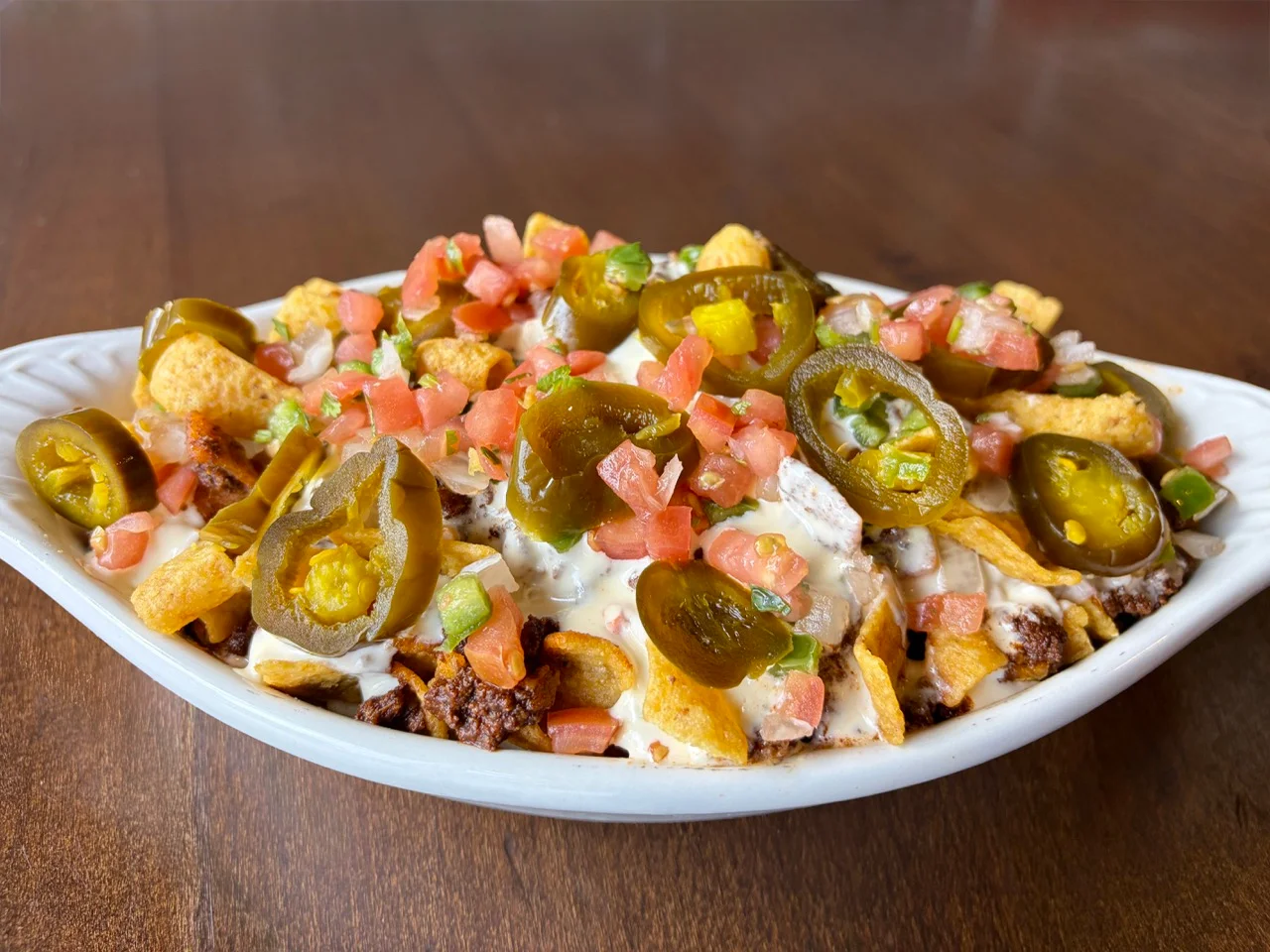 A serving of nachos topped with jalapeños, diced tomatoes, and a creamy sauce, served in a white dish.