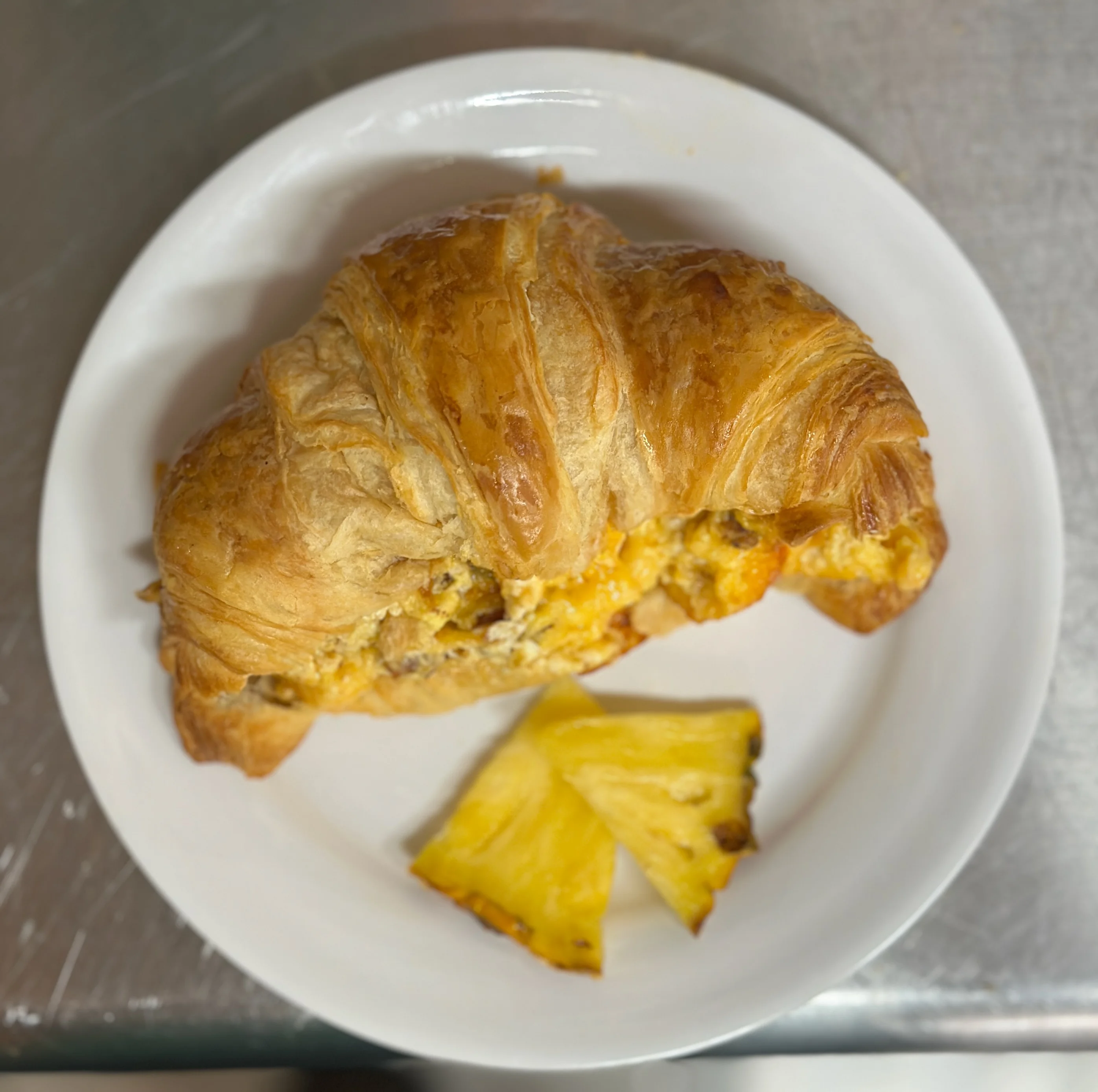 A breakfast croissant paired with slices of pineapple