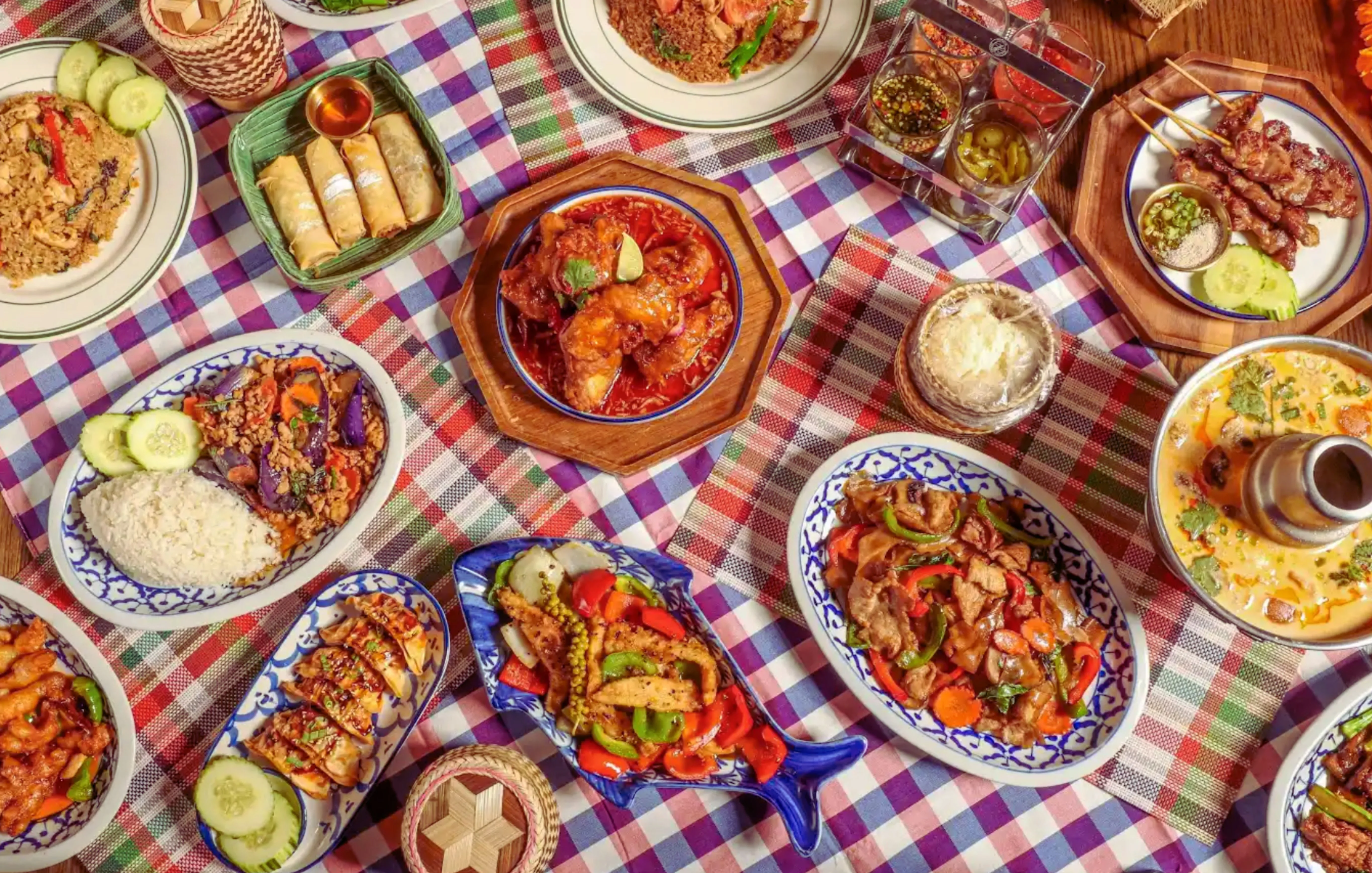 Assorted Thai dishes including pad thai and curry on a checkered tablecloth