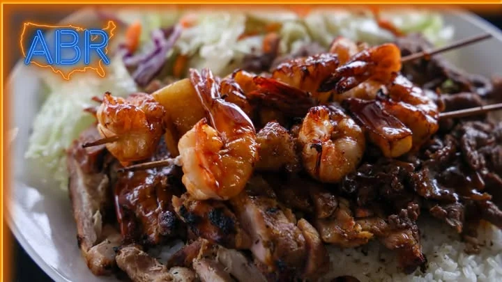 A plate of grilled chicken and shrimp skewers served on a bed of rice, accompanied by fresh vegetables.