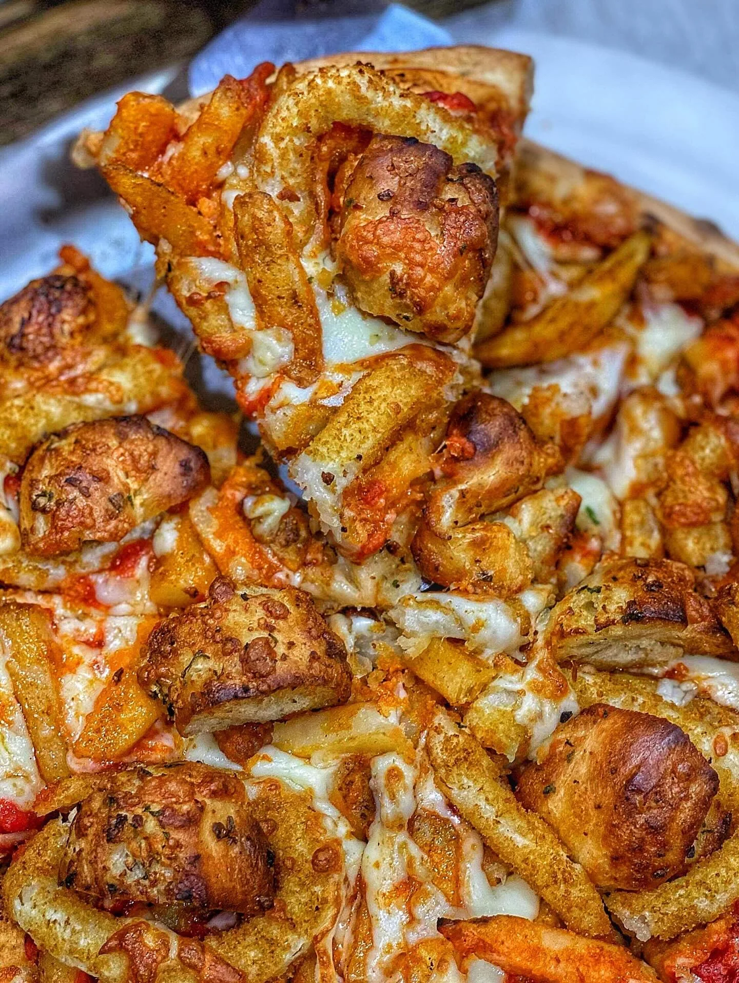 A slice of pizza topped with golden fried potatoes and chewy bread bites, all melted into a cheesy mixture.