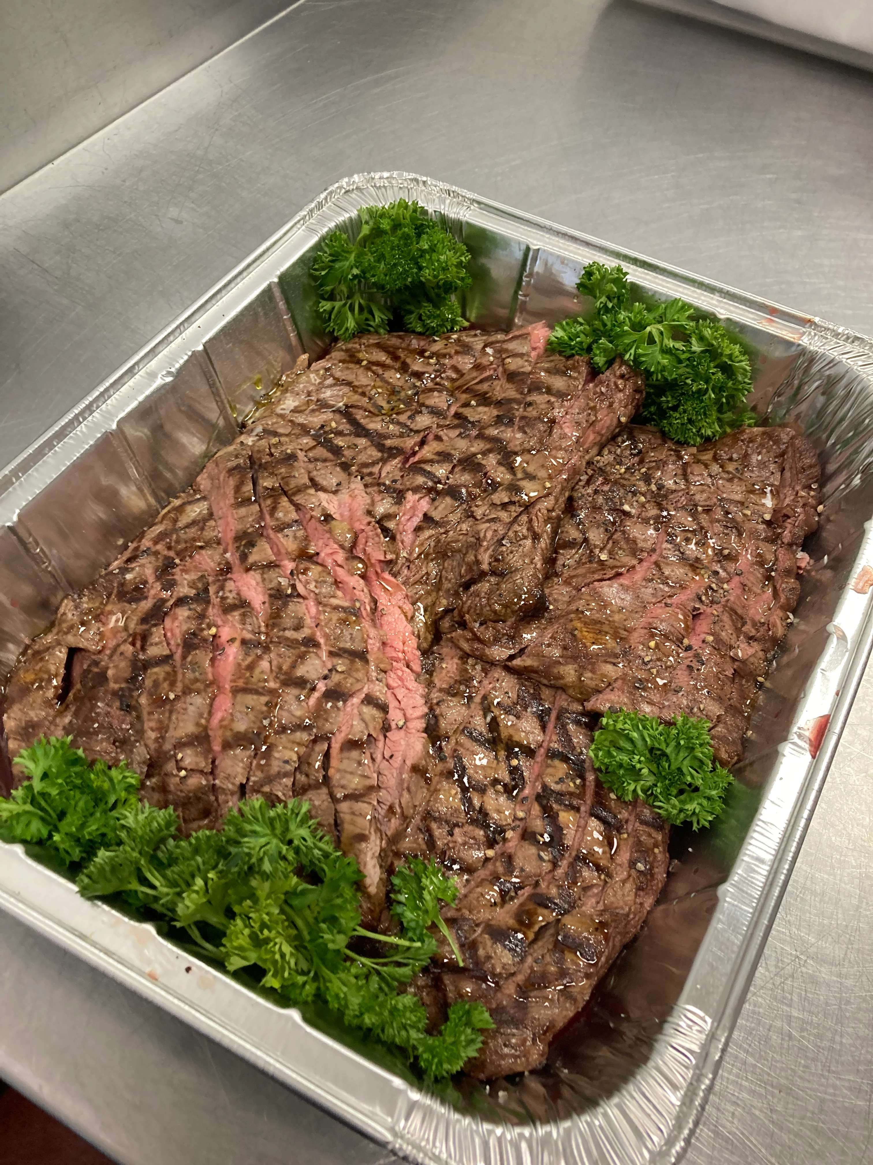 Grilled steak slices garnished with parsley in a metal tray.