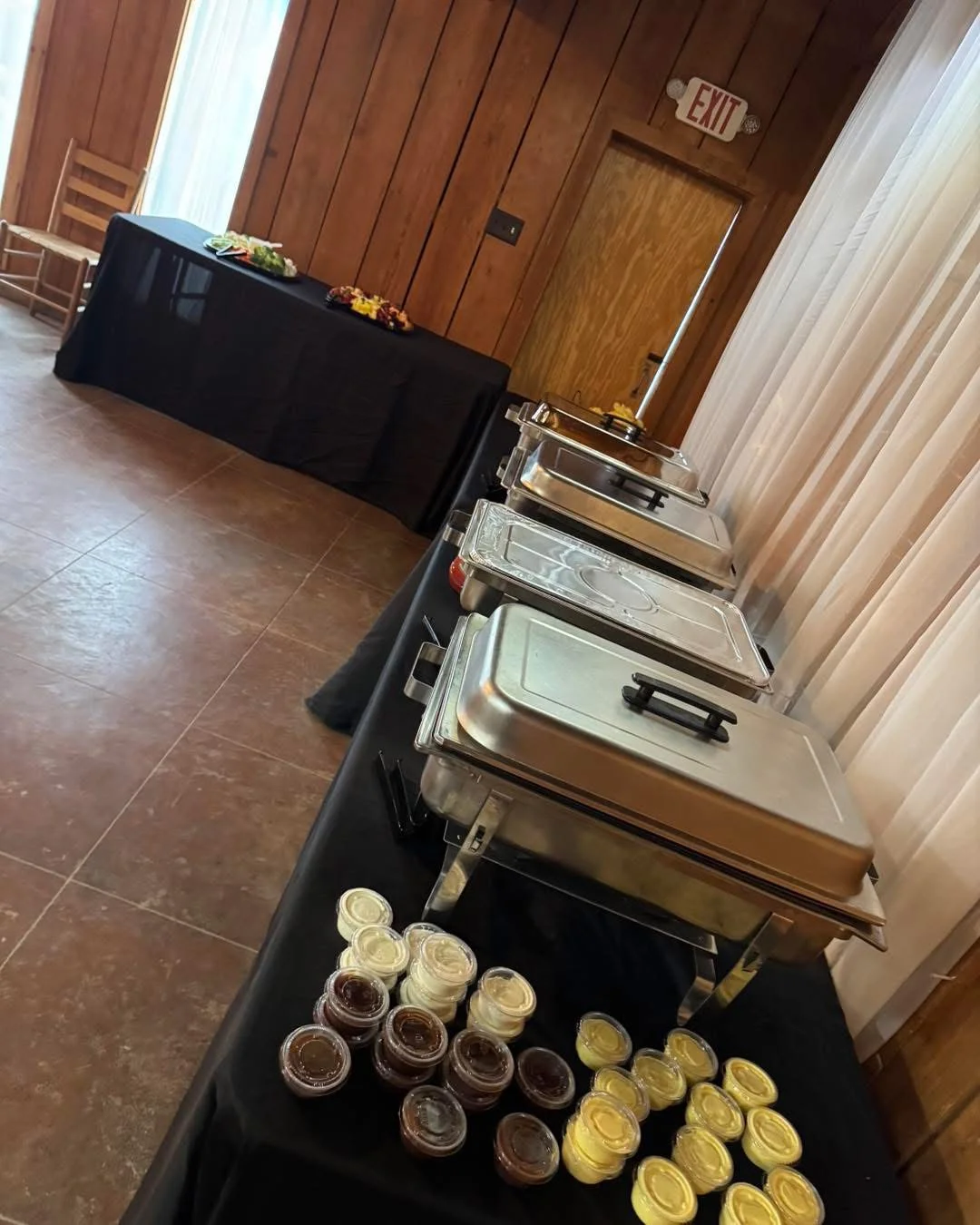 Catered buffet setup with chafing dishes and sauces in a wood-paneled dining room