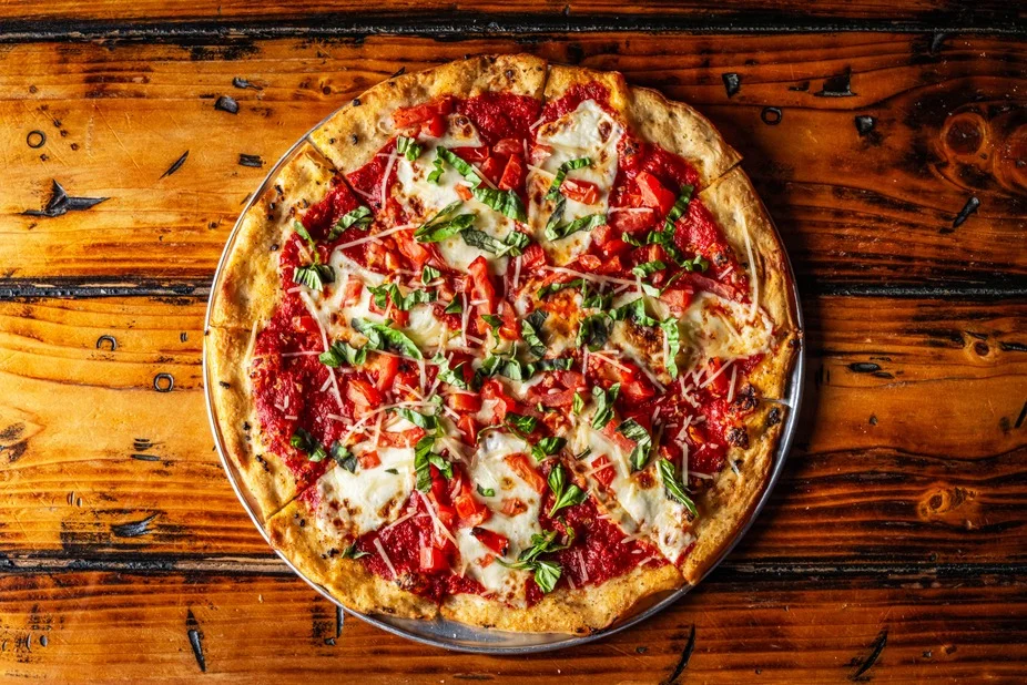 A large pizza topped with drizzles of sauce, pickles, and pieces of crispy bacon, served on a wooden table.