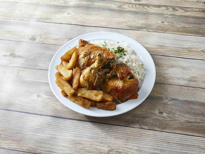 Plate of roasted chicken with fries and rice on a wooden table.