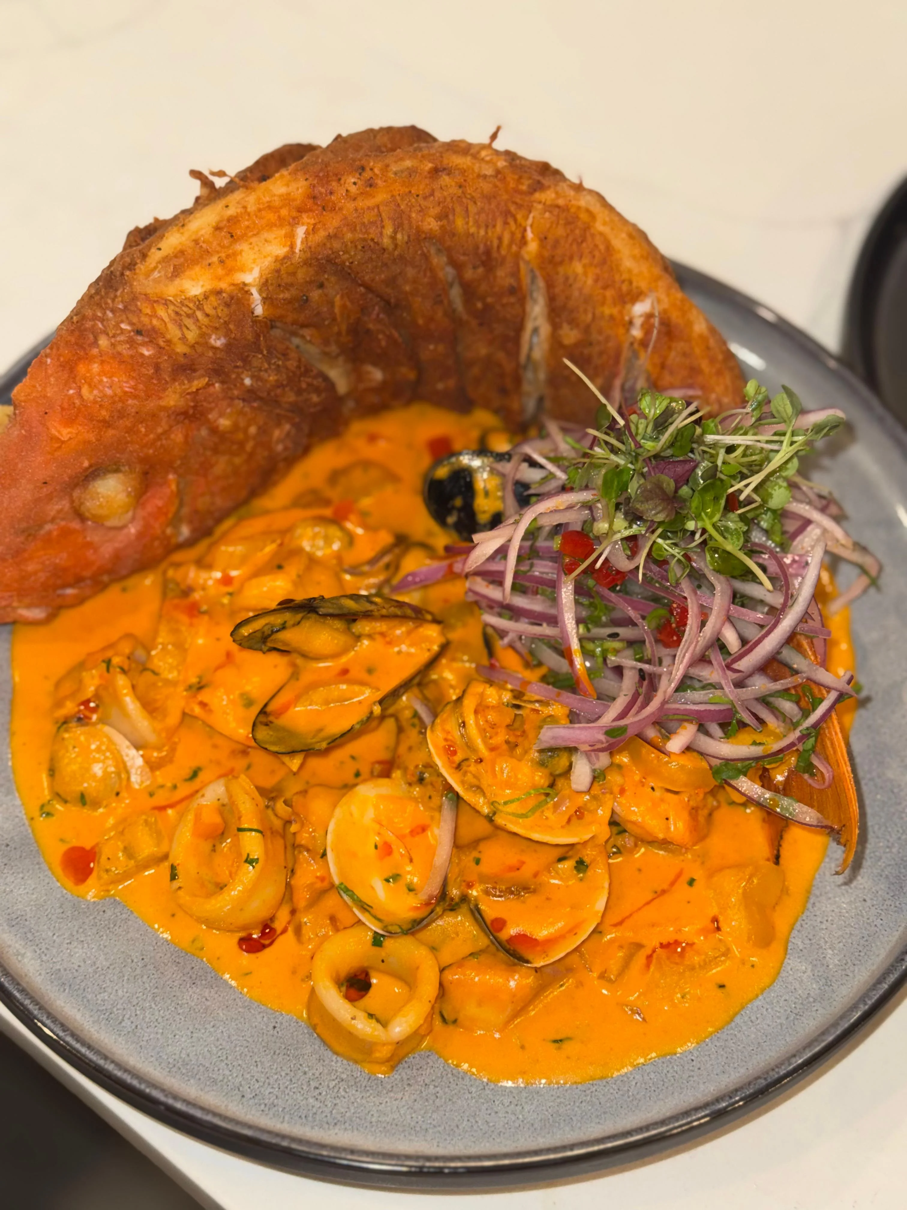 A plate showcasing a beautifully designed seafood dish with a crispy fish head, mixed seafood in a rich orange sauce, and a side of fresh vegetables.