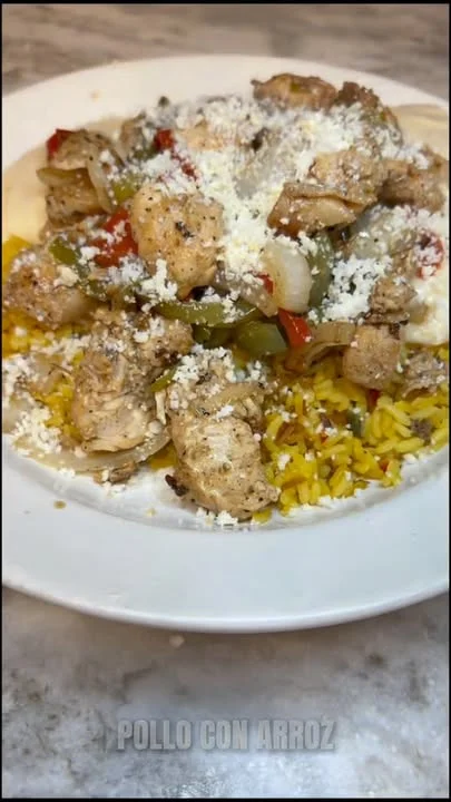 A plate of chicken and sautéed vegetables over yellow rice, topped with cheese. The combination offers a hearty and flavorful meal that highlights Mexican culinary traditions.