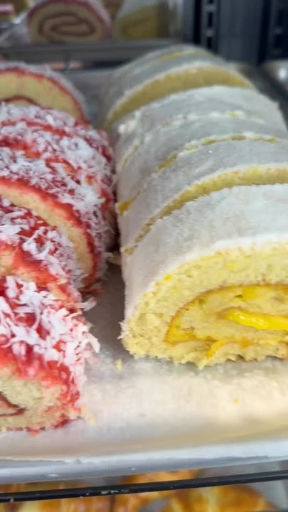 Two types of roll cakes displayed in a bakery. One is coated with red icing and coconut, while the other is a lemon-flavored roll.