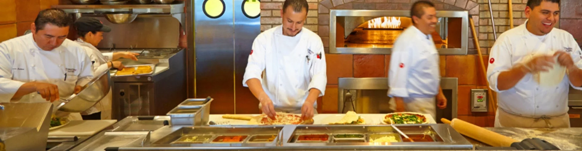 Restaurant chef preparing a pizza while another plates a salad and another cook cutting fresh baked bread