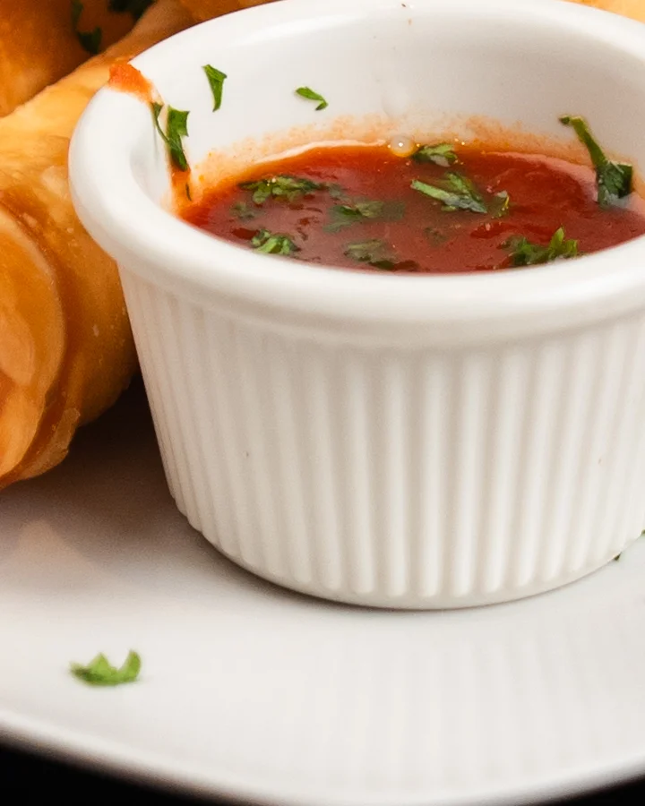 Two golden-brown arancini balls served on a plate with marinara sauce and a sprinkle of cheese.