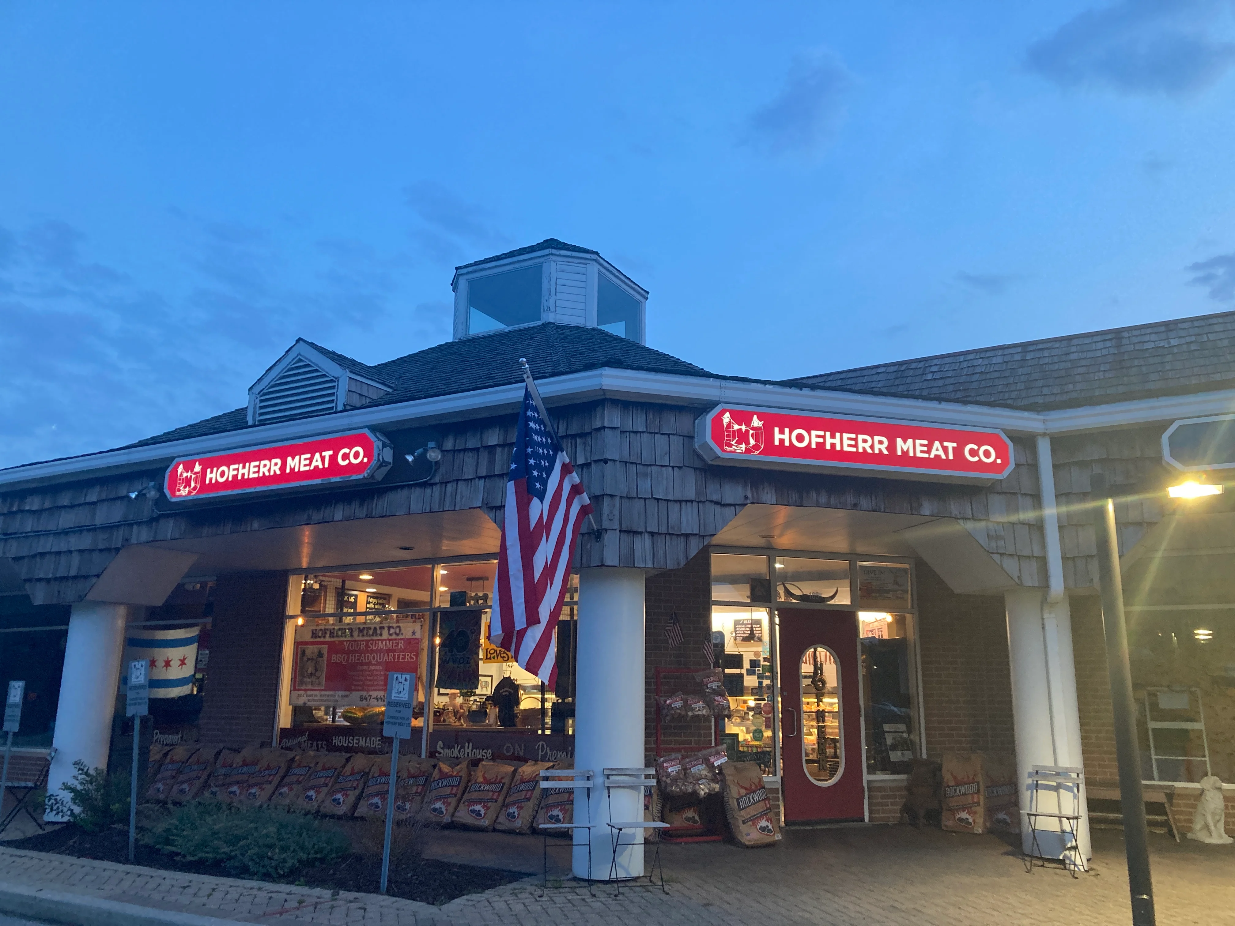 Exterior of Hofherr Meat Co. with American flag at dusk.