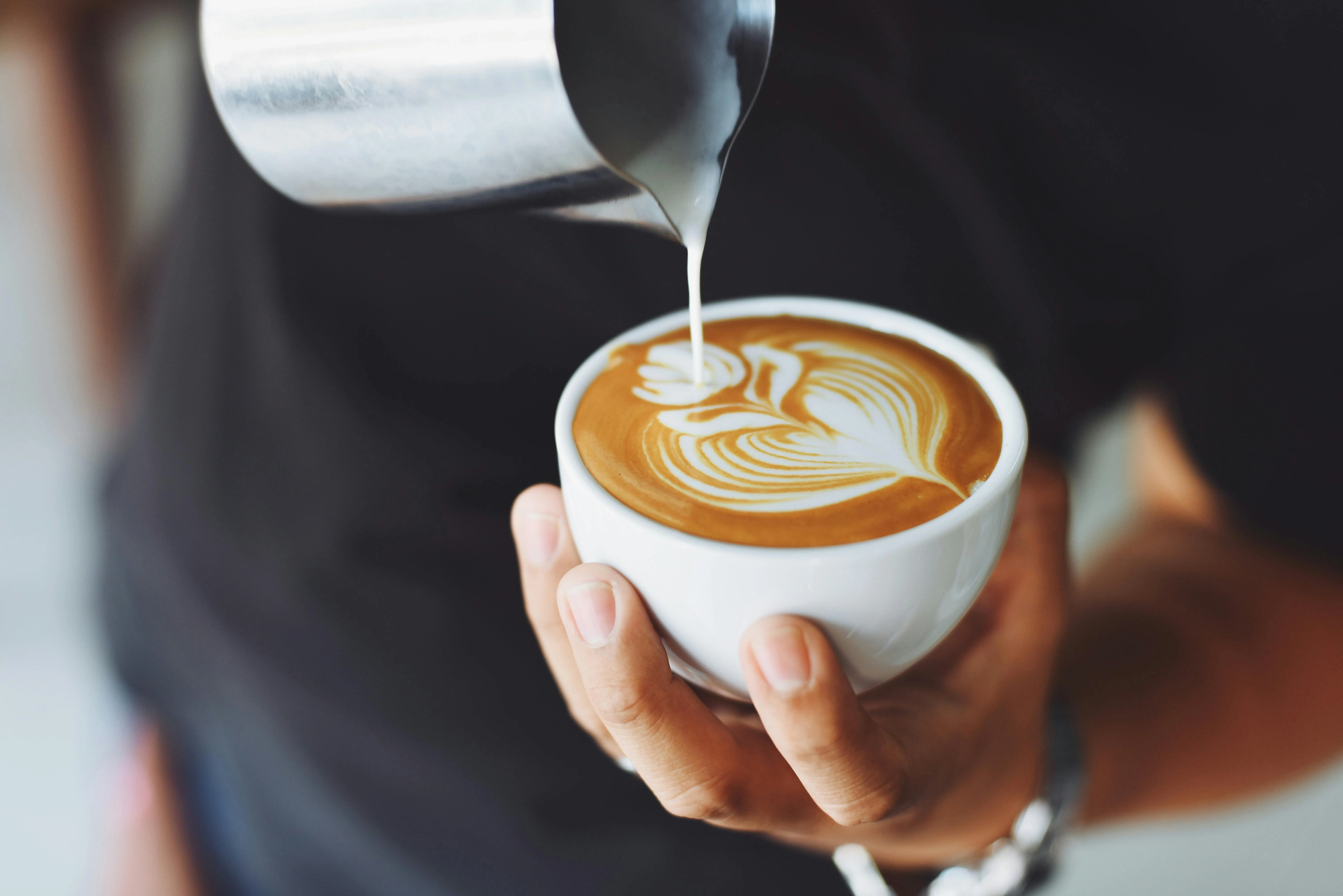 Barista pouring latte art into a white cup