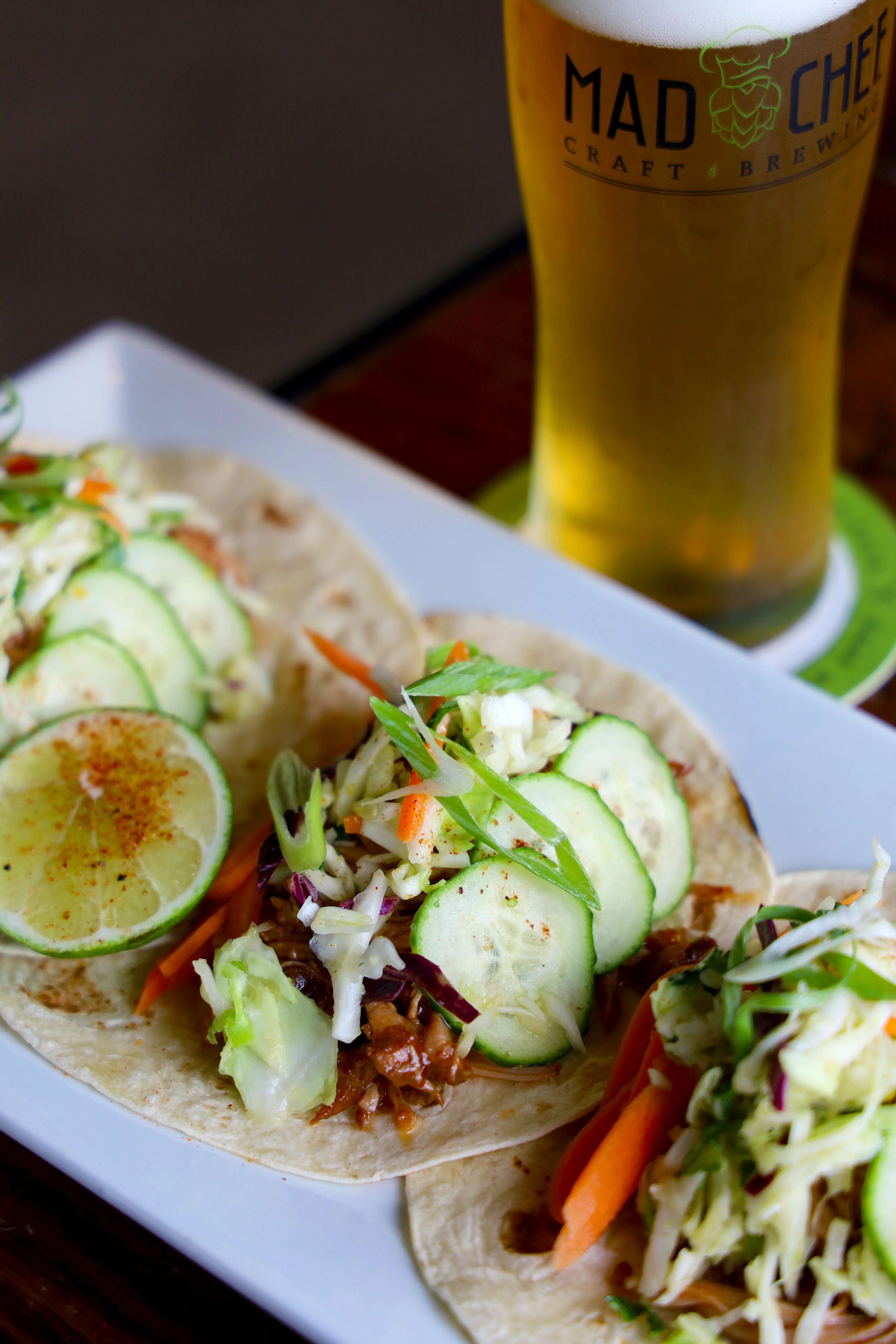 Three tacos with pulled meat, pineapple, and lime on a plate.