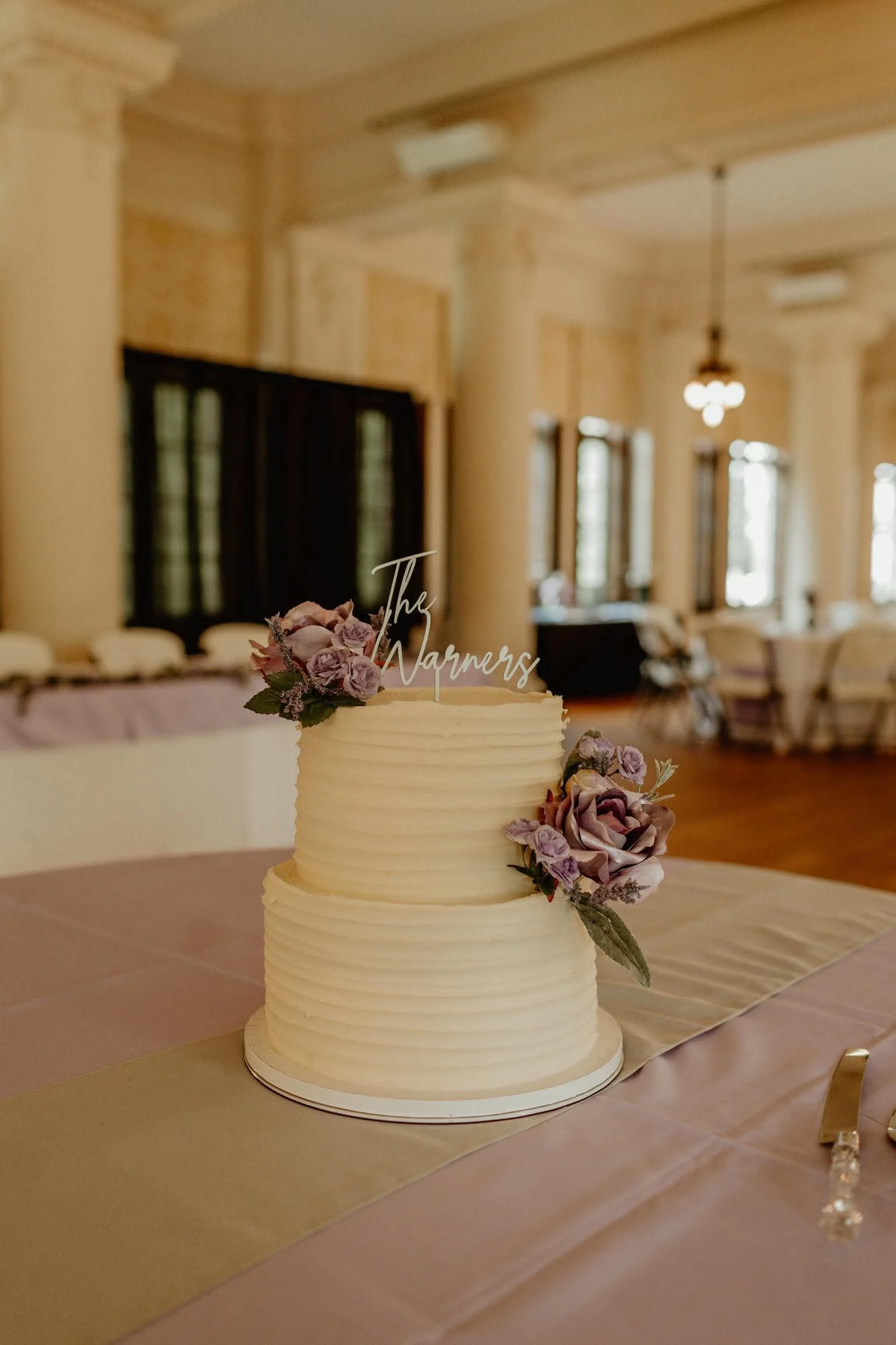 Elegant wedding cake adorned with purple flowers and a personalized topper