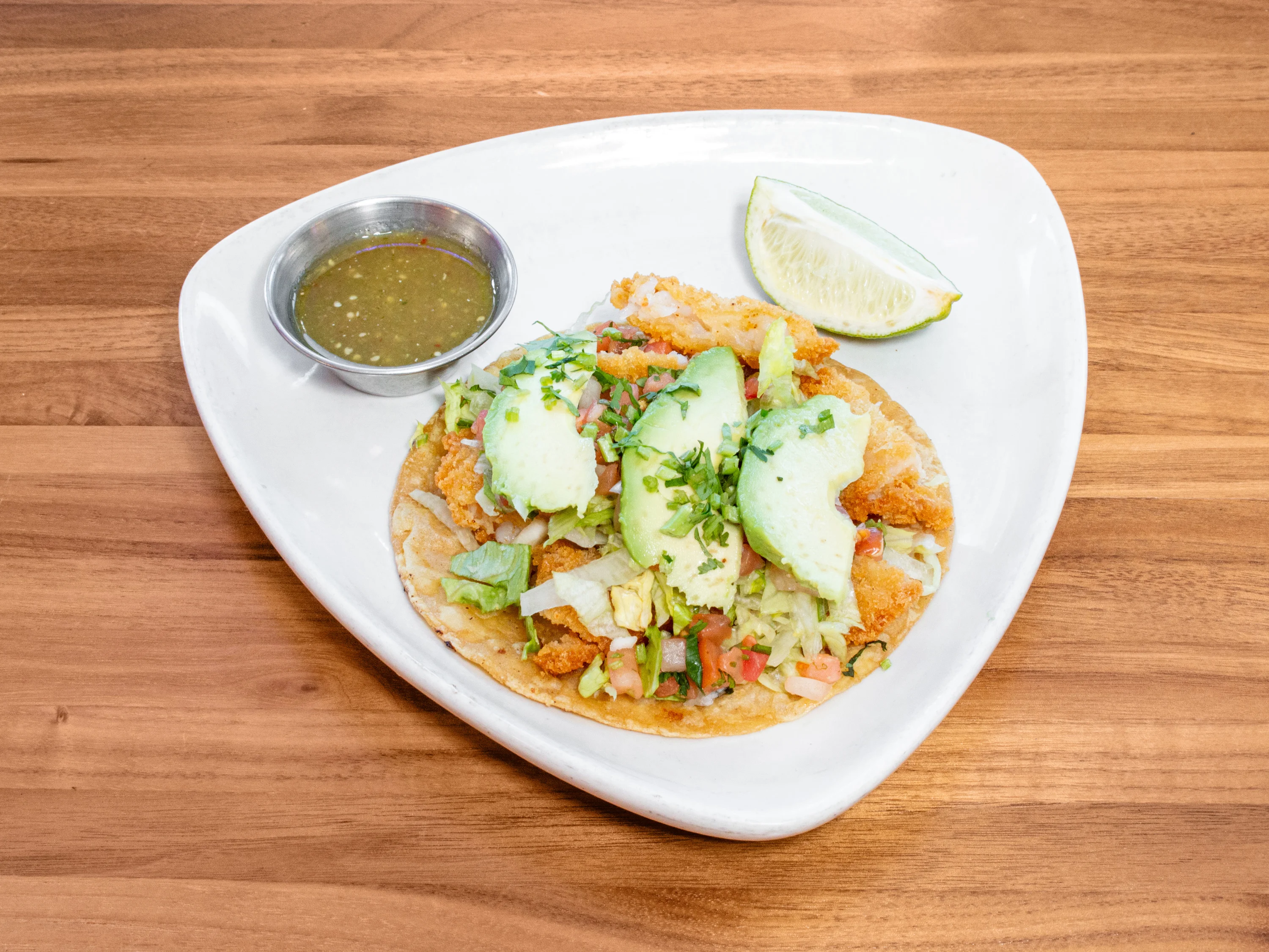 Crunchy shrimp taco topped with fresh ingredients and served on a plate.