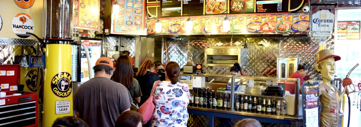 Busy restaurant interior with colorful menu and patrons in line