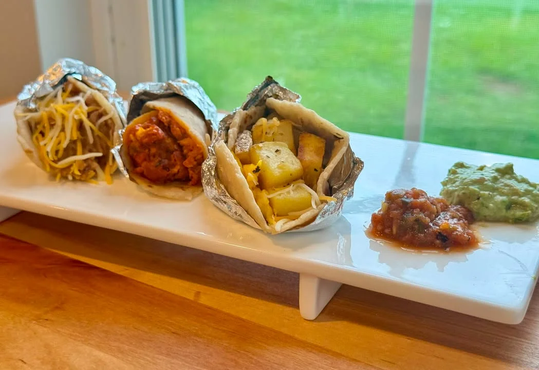 Three delicious burritos served with salsa and guacamole on a white platter