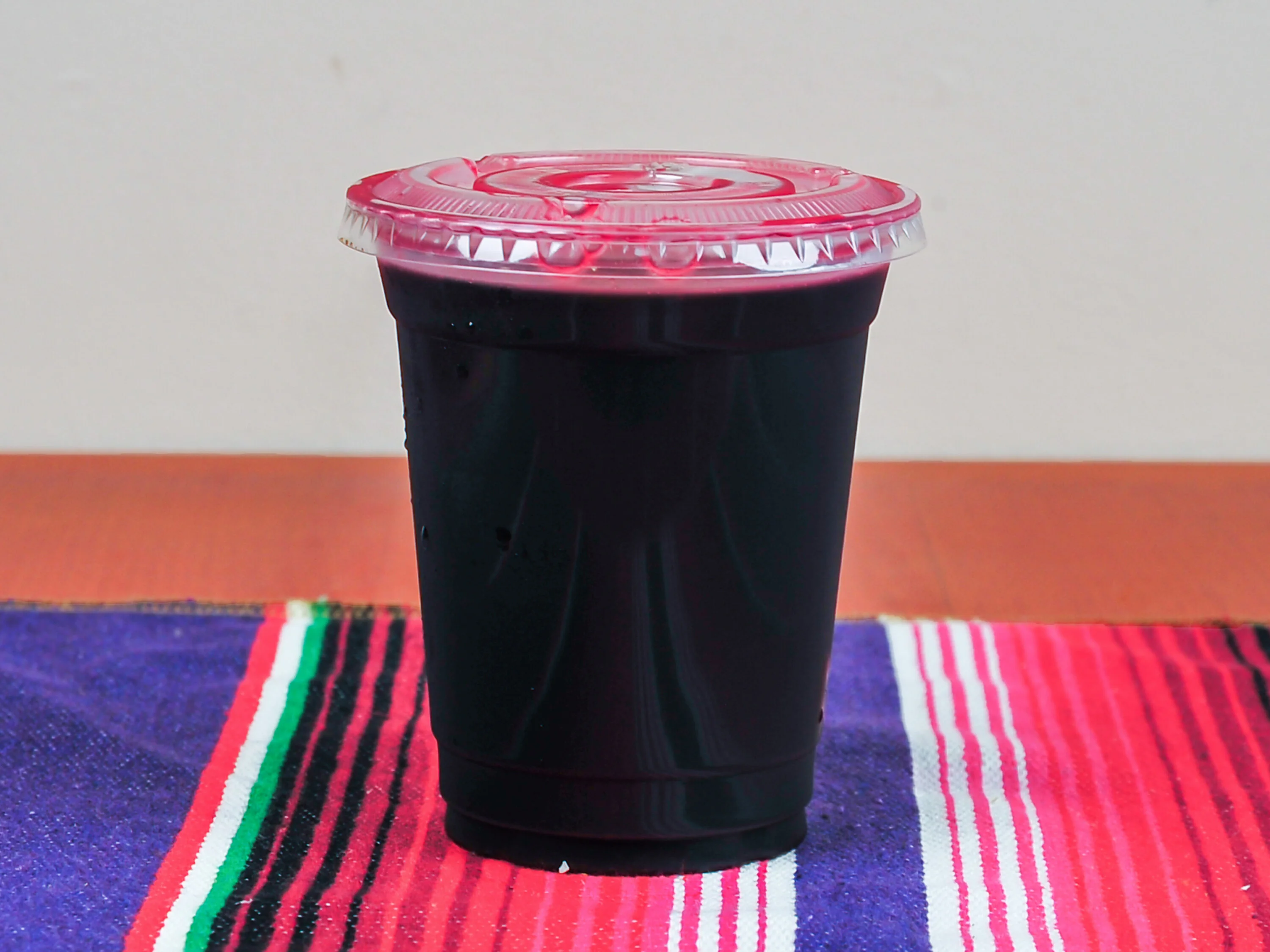 A cup filled with a dark beverage, possibly a fruit drink or soda, featuring a clear lid.