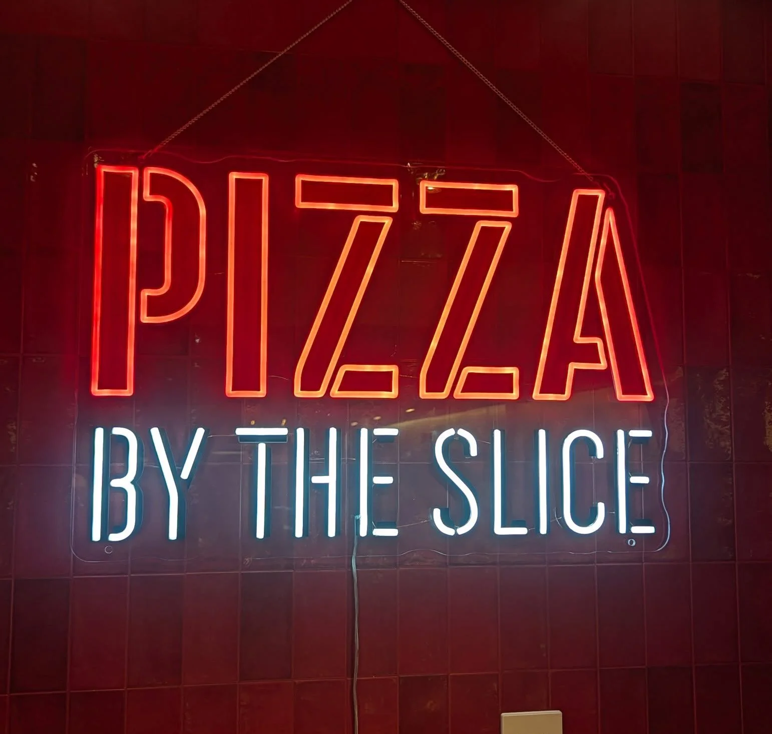 Neon sign reading 'Pizza by the Slice' in a cozy restaurant