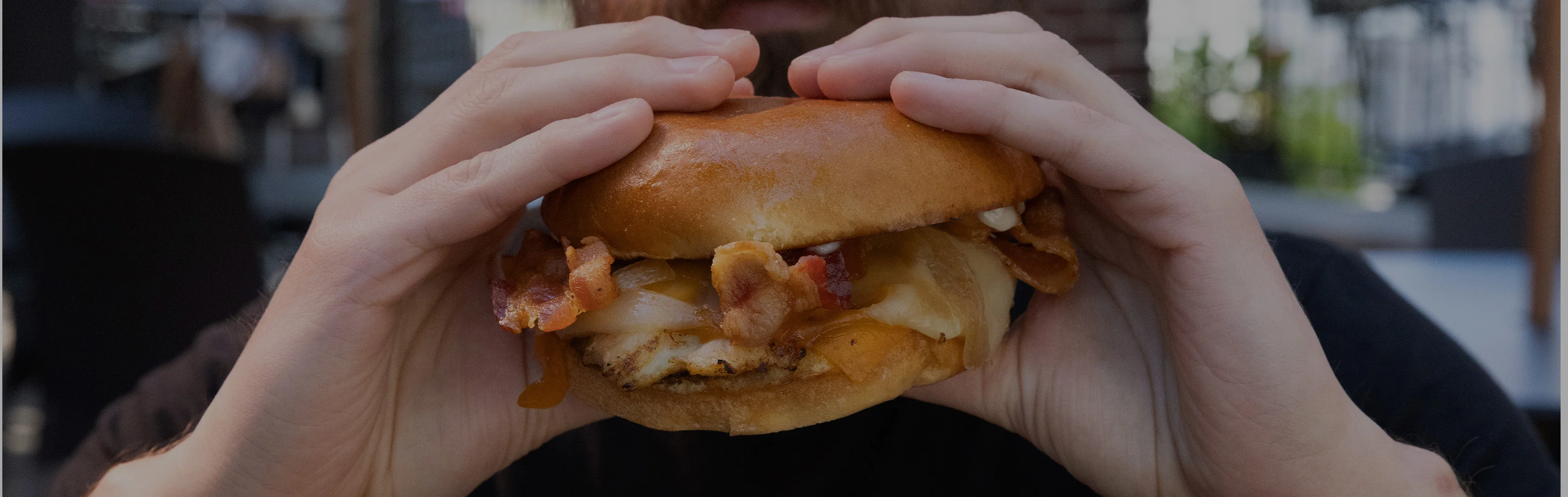 Juicy bacon cheeseburger held in hands, showcasing a delicious sandwich experience