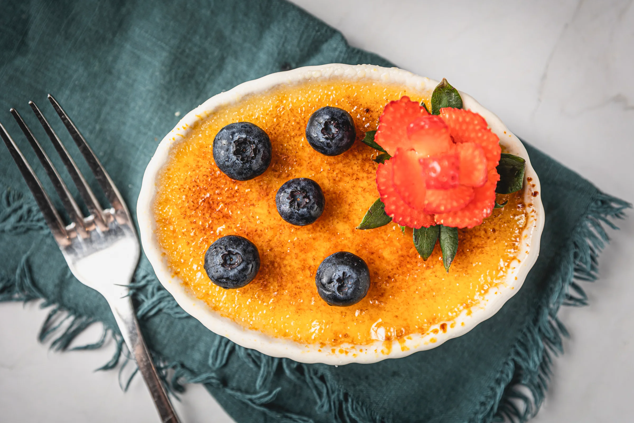 Classic French crème brûlée with blueberries and edible flower garnish
