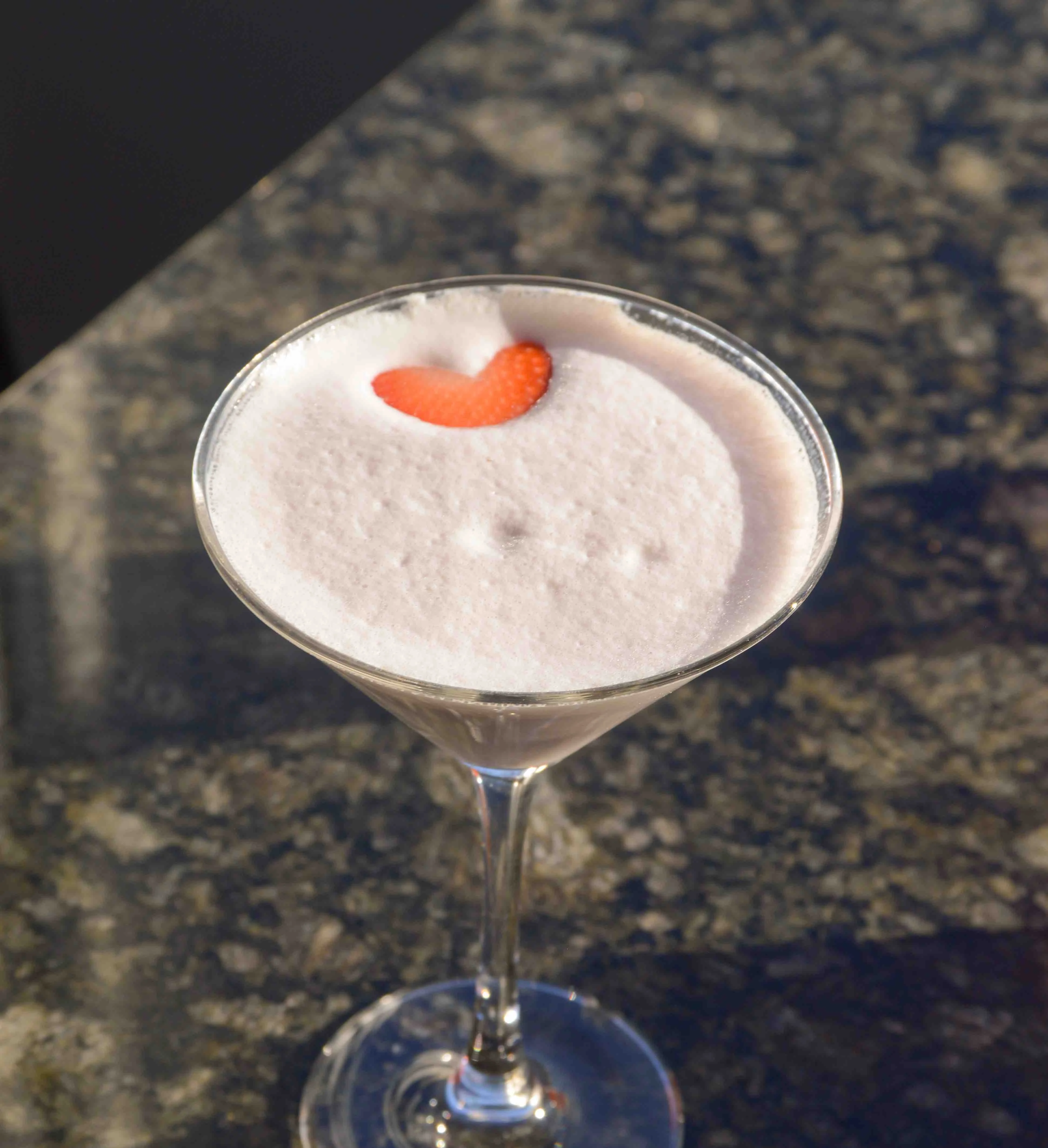 Be Mine Martini on a table in the sunlight with a heart-shaped strawberry slice floated on the top of the cocktail