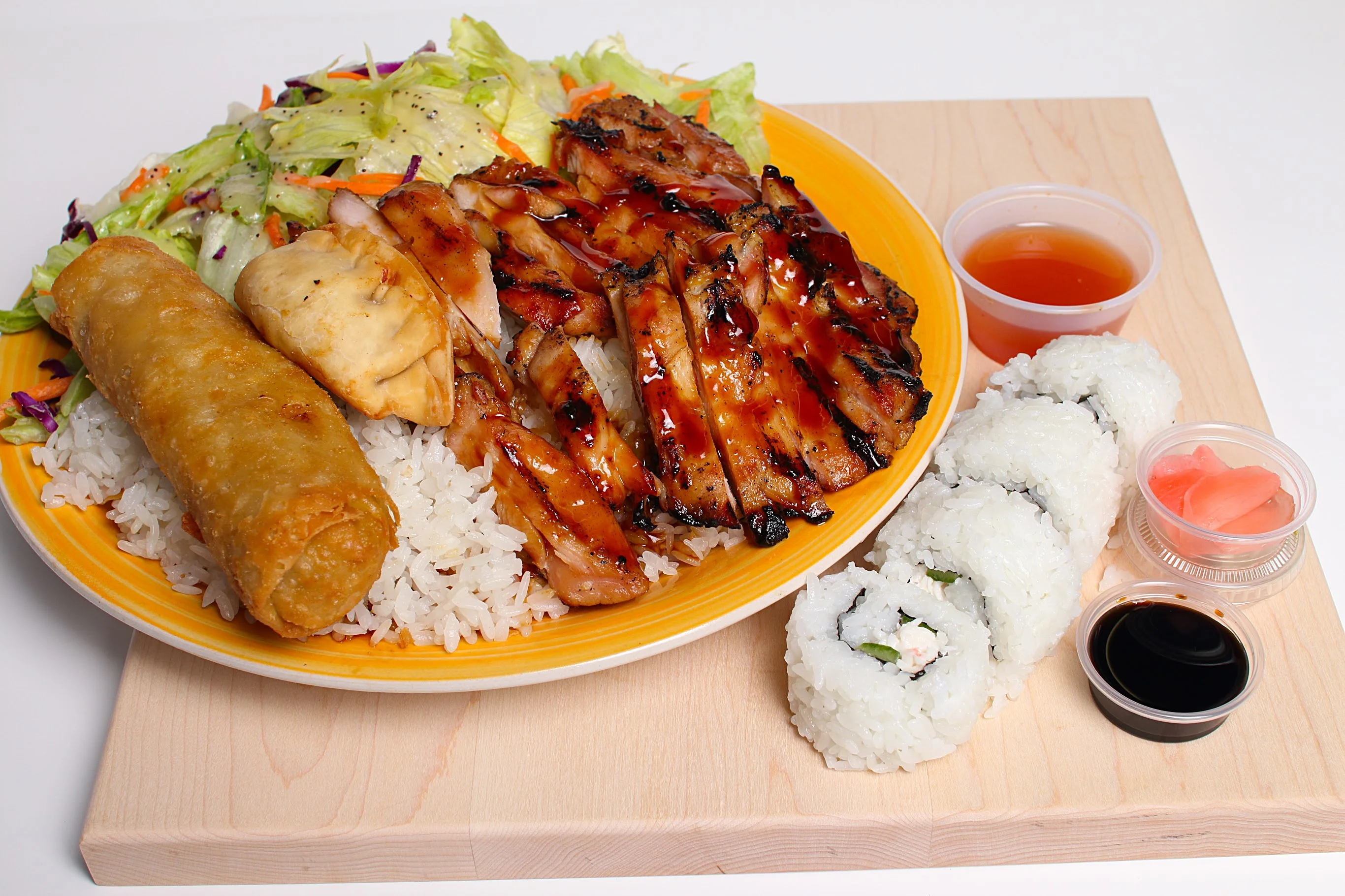 A meal box containing rice topped with grilled chicken, cabbage, and carrots, accompanied by salad and two containers of dipping sauce.