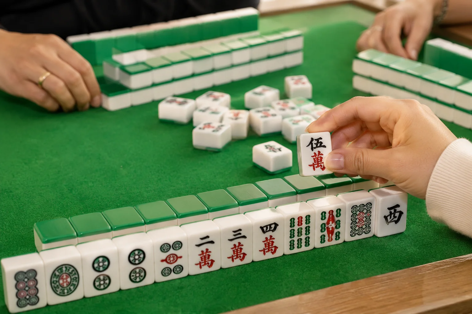 Players engaging in a game of Mahjong on a green felt table