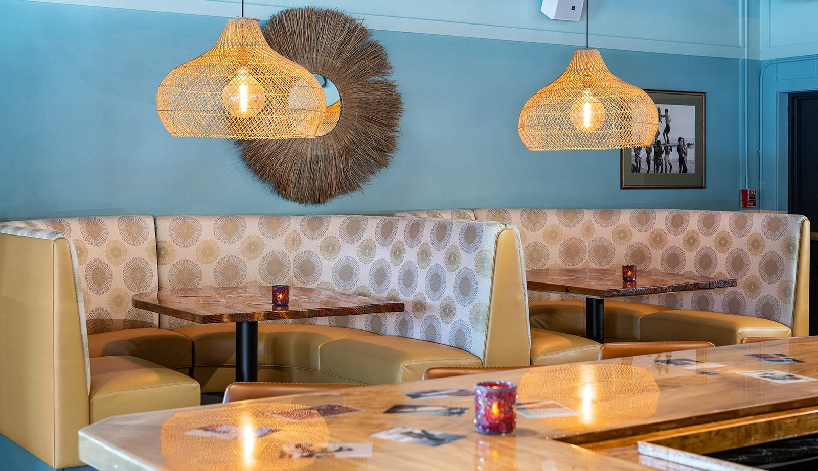 Stylish restaurant dining room with blue walls, banquettes, and woven pendant lights