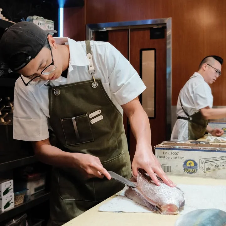 A chef skillfully preparing fish in a professional kitchen setting.