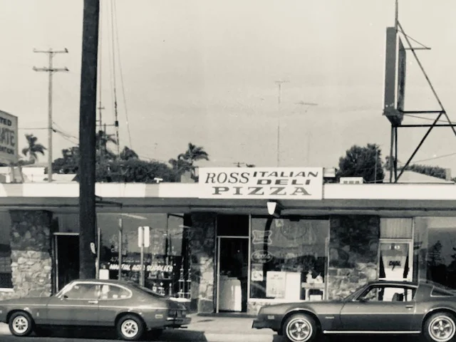 Exterior view of Ross Italian Deli Pizza with vintage cars parked outside.