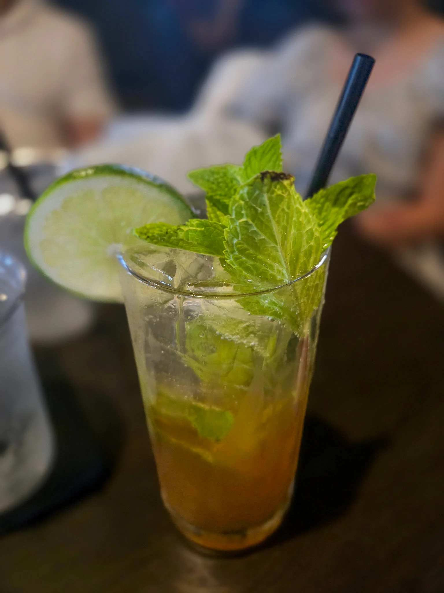 A refreshing cocktail served in a tall glass with mint leaves and a lime slice, placed on a dark surface.