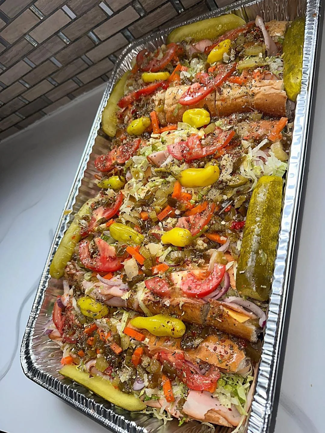 A tray filled with sandwiches topped with layers of shredded lettuce, tomatoes, peppers, and pickles. The sandwiches are garnished with a mix of seasonings.