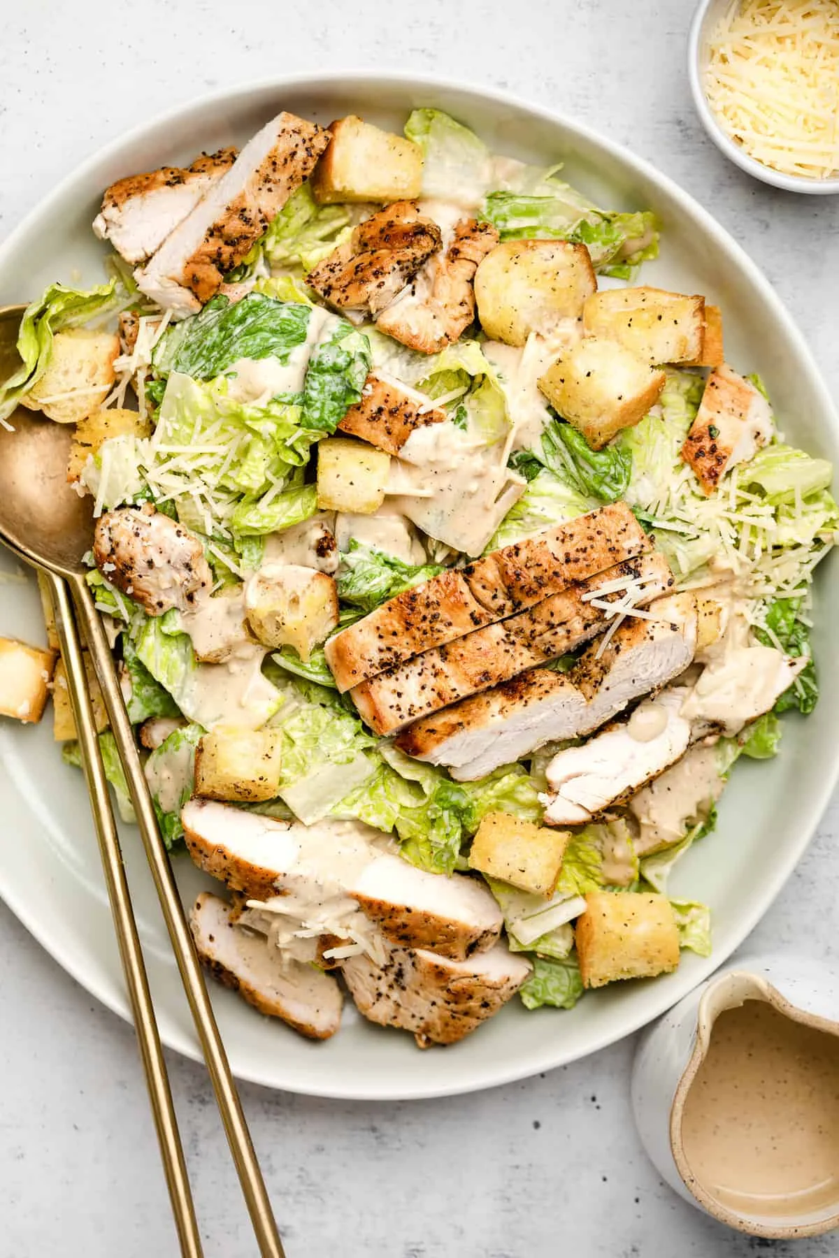 A generous serving of grilled chicken salad featuring romaine lettuce, croutons, and parmesan cheese, drizzled with a creamy dressing.
