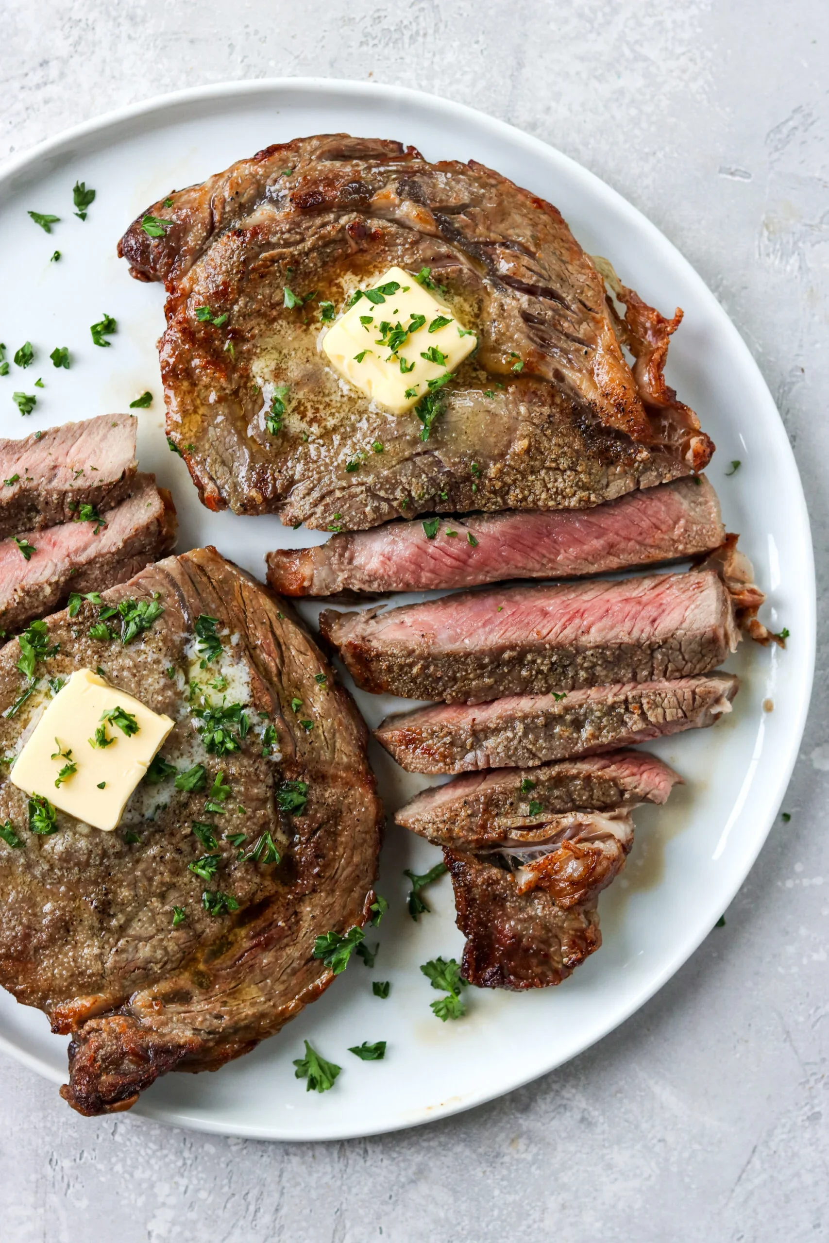 Juicy ribeye steak with butter and herbs on a white plate