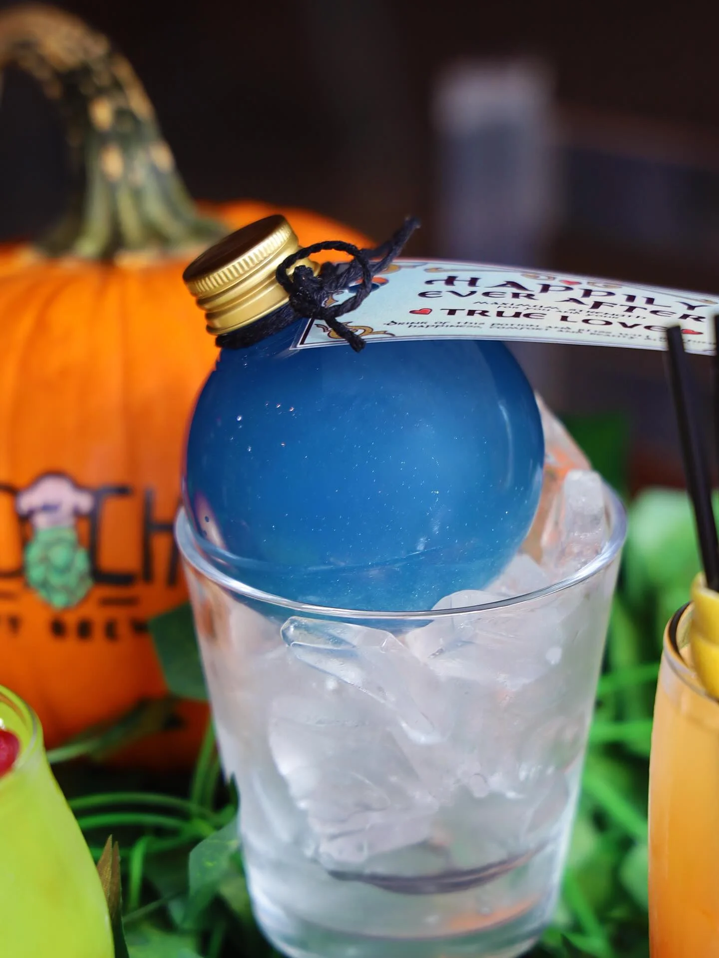 Colorful cocktail served in a glass with ice and a decorative pumpkin in the background