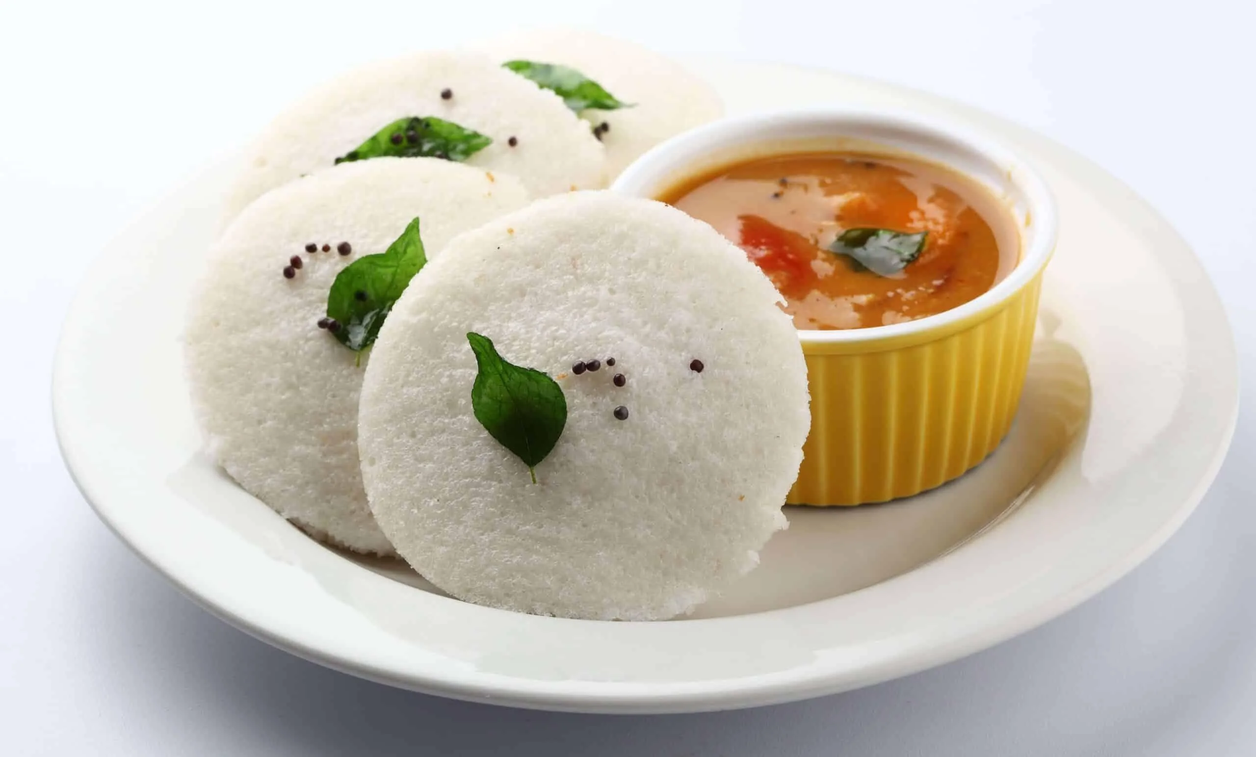 Three soft idlis accompanied by a bowl of sambar, featuring spices and vegetables.