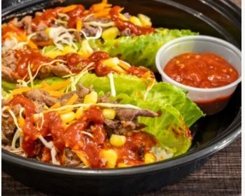 Three tacos filled with beef, shredded cheese, lettuce, and corn, garnished with salsa and served in a black container.
