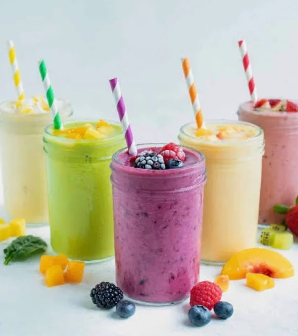 Colorful assortment of smoothies in clear cups with fresh fruit garnishes.
