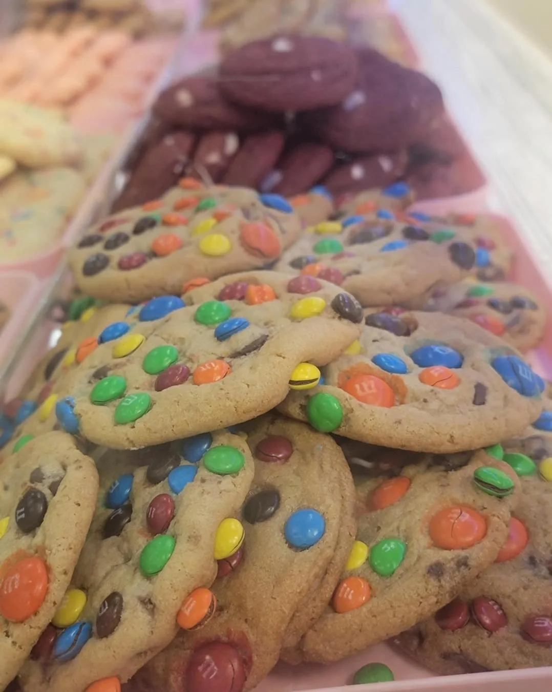 Trays of assorted cookies, including cookies topped with colorful M&M candies, chocolate chip cookies, and Oreo-style cookies.