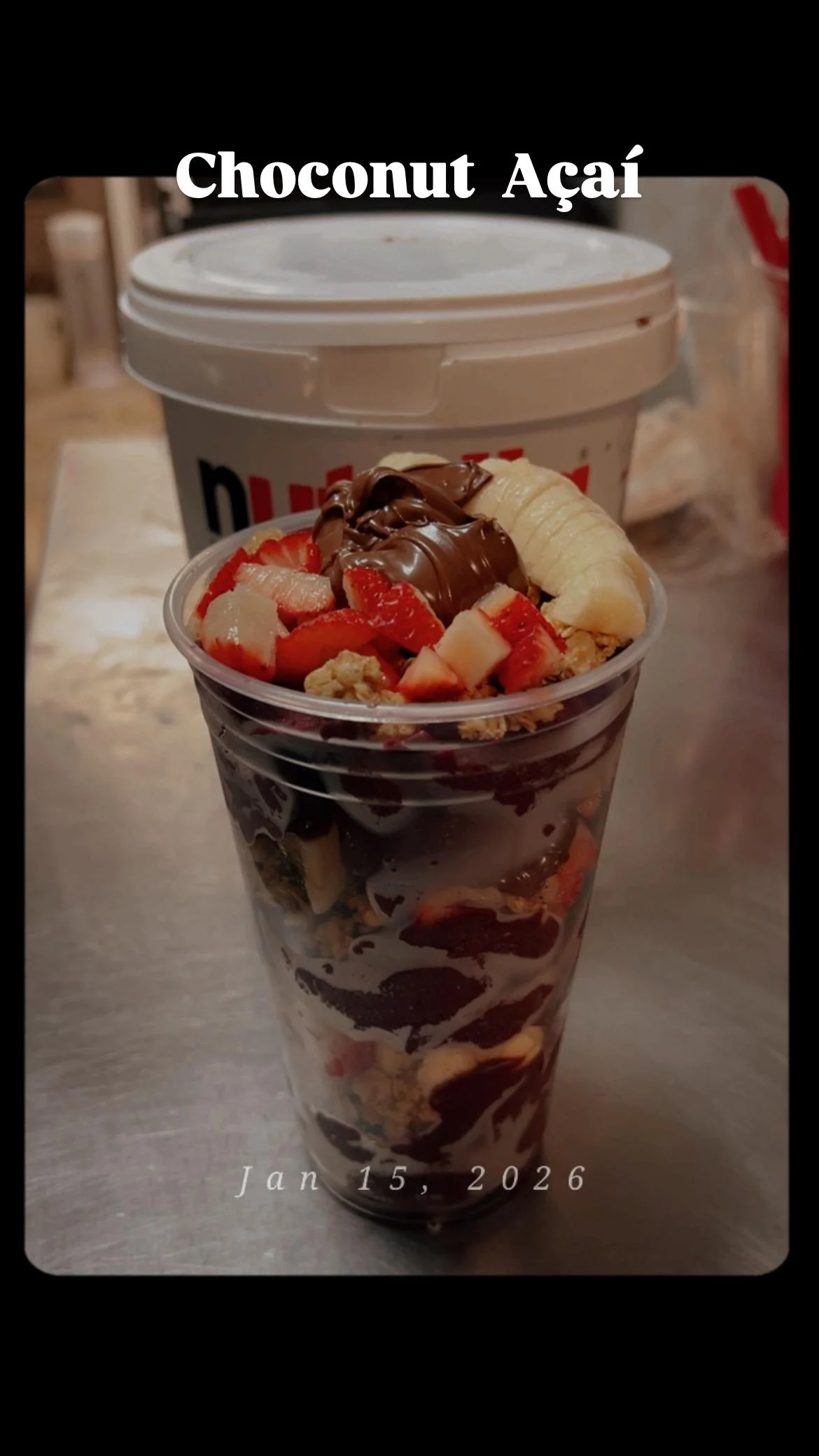 A cup of Choconut Açaí topped with chocolate, fresh fruits, and granola, presented against a simple background.