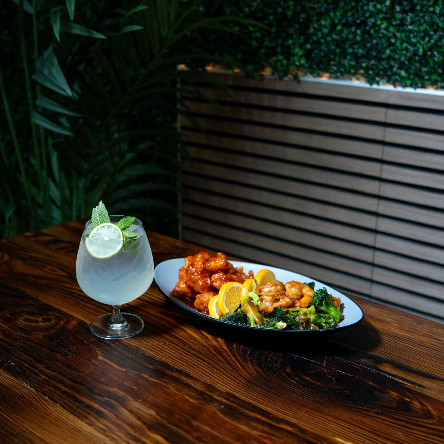 Plate of orange chicken with broccoli and a refreshing cocktail in a restaurant setting