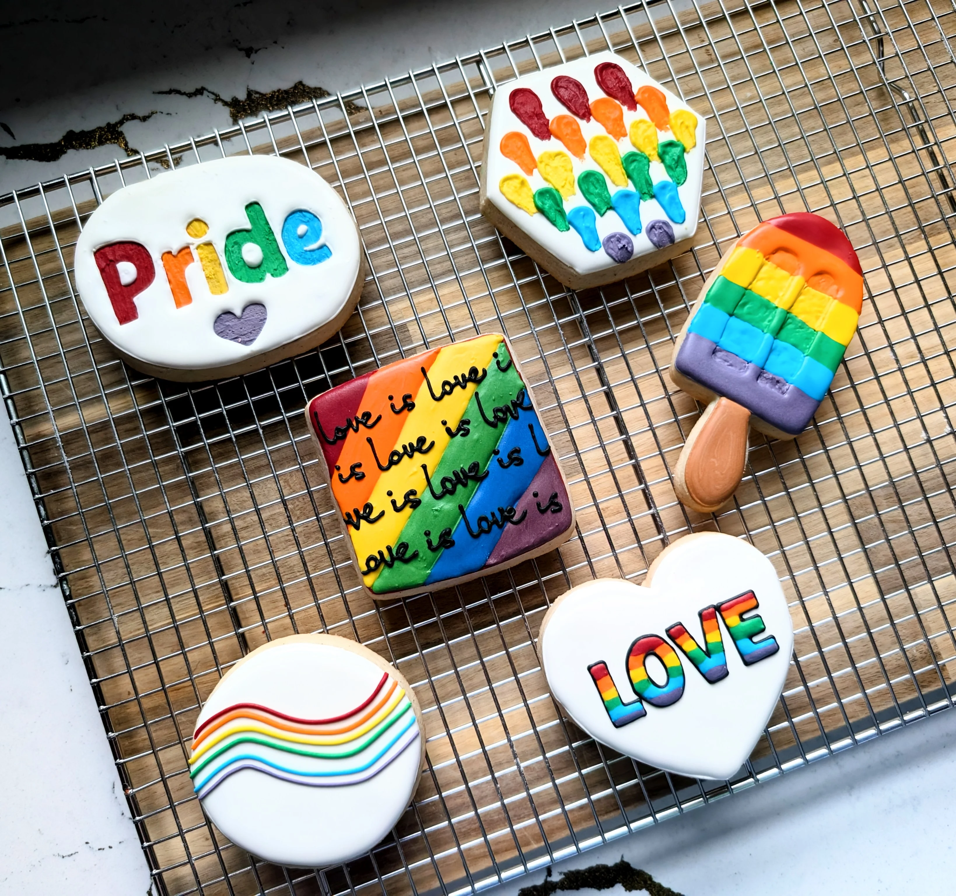 Colorful decorated cookies with pride themes on a cooling rack.