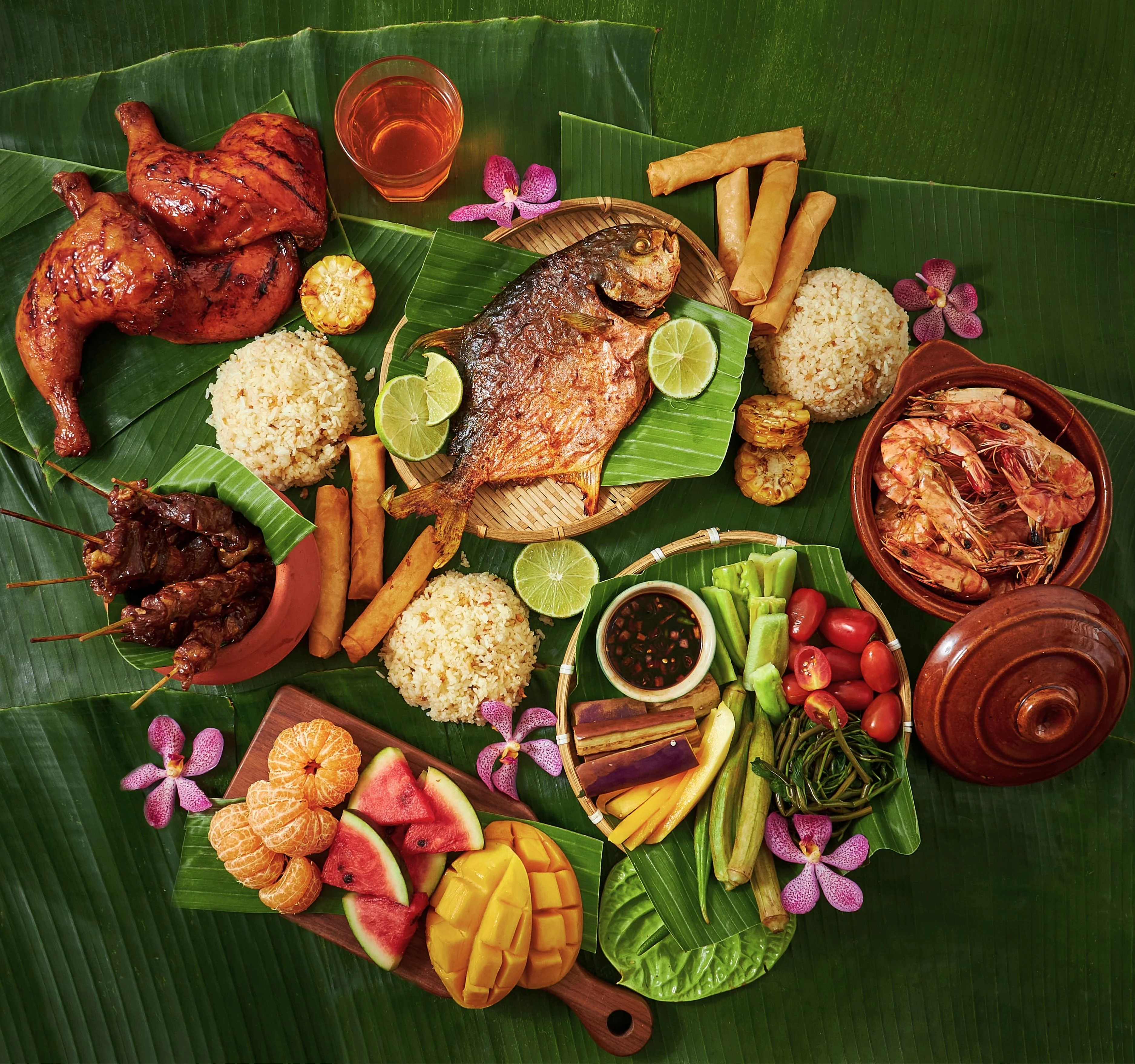 Filipino kamayan feast with grilled chicken, fish, rice, lumpia, and tropical fruit