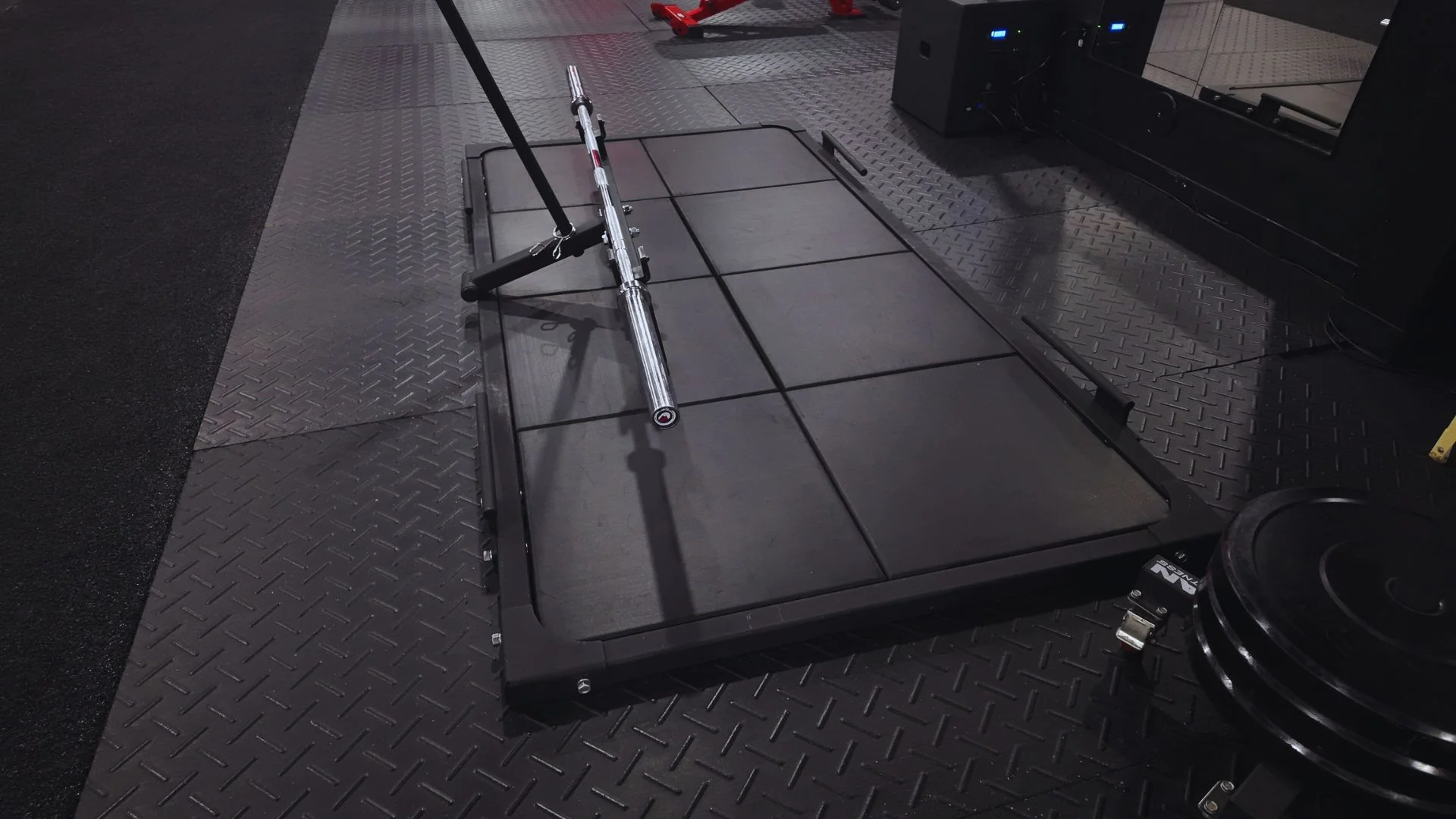 A gym floor showing a barbell on a platform, with diamond-patterned rubber flooring, ideal for weightlifting.