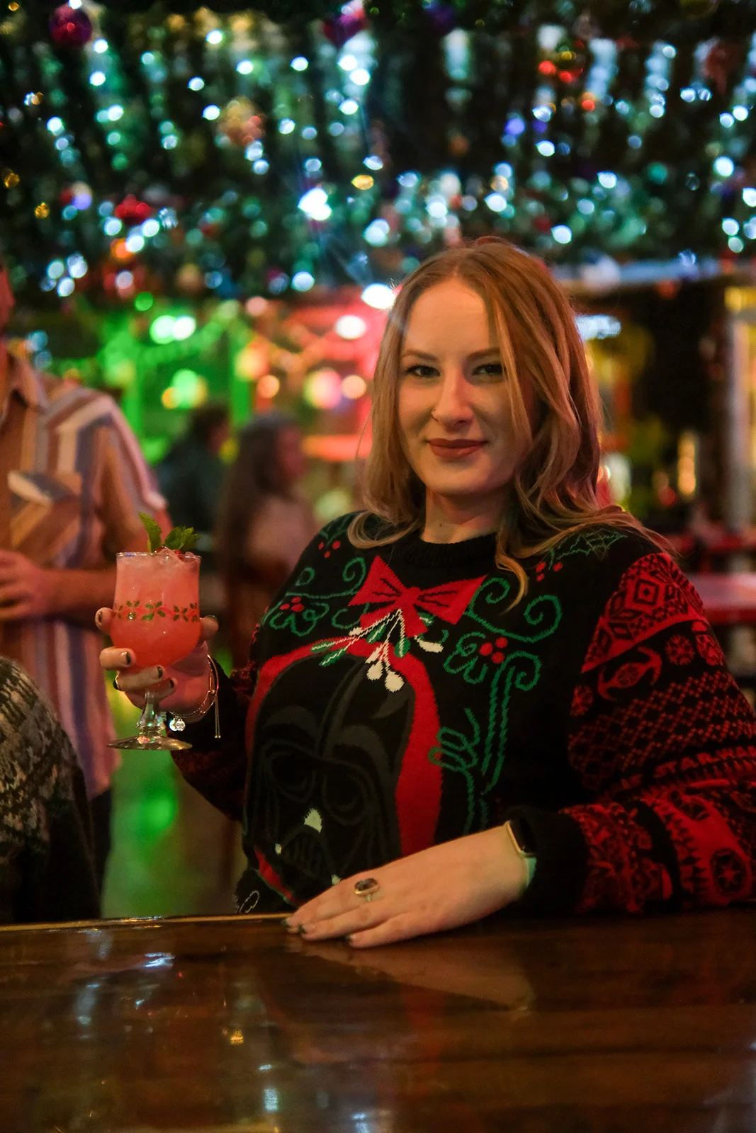 Woman in festive sweater holding a cocktail at a vibrant bar
