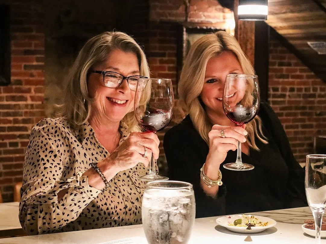 Two women toasting with red wine glasses in a cozy restaurant setting