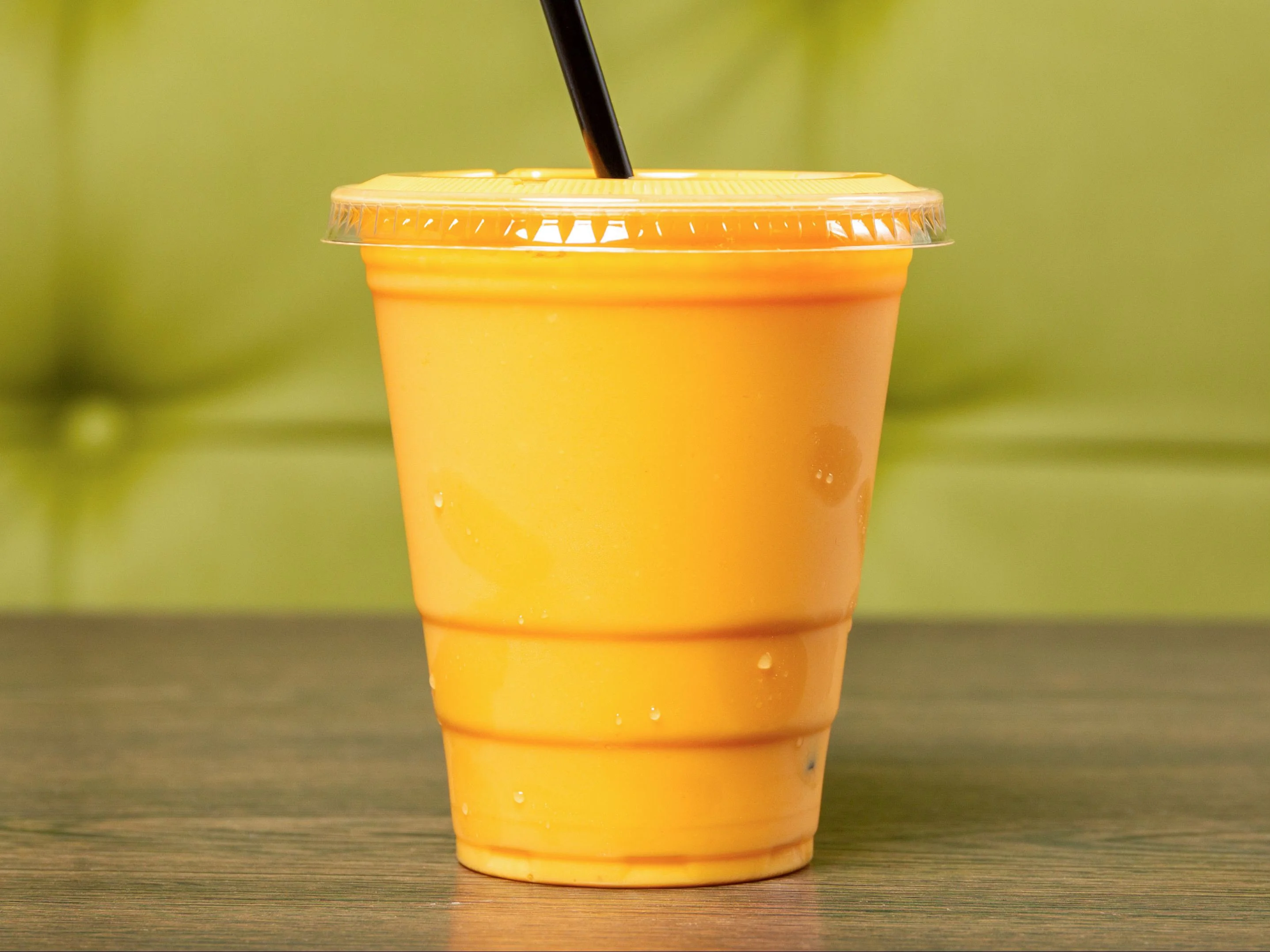 A cup filled with an orange beverage, set against a green background.